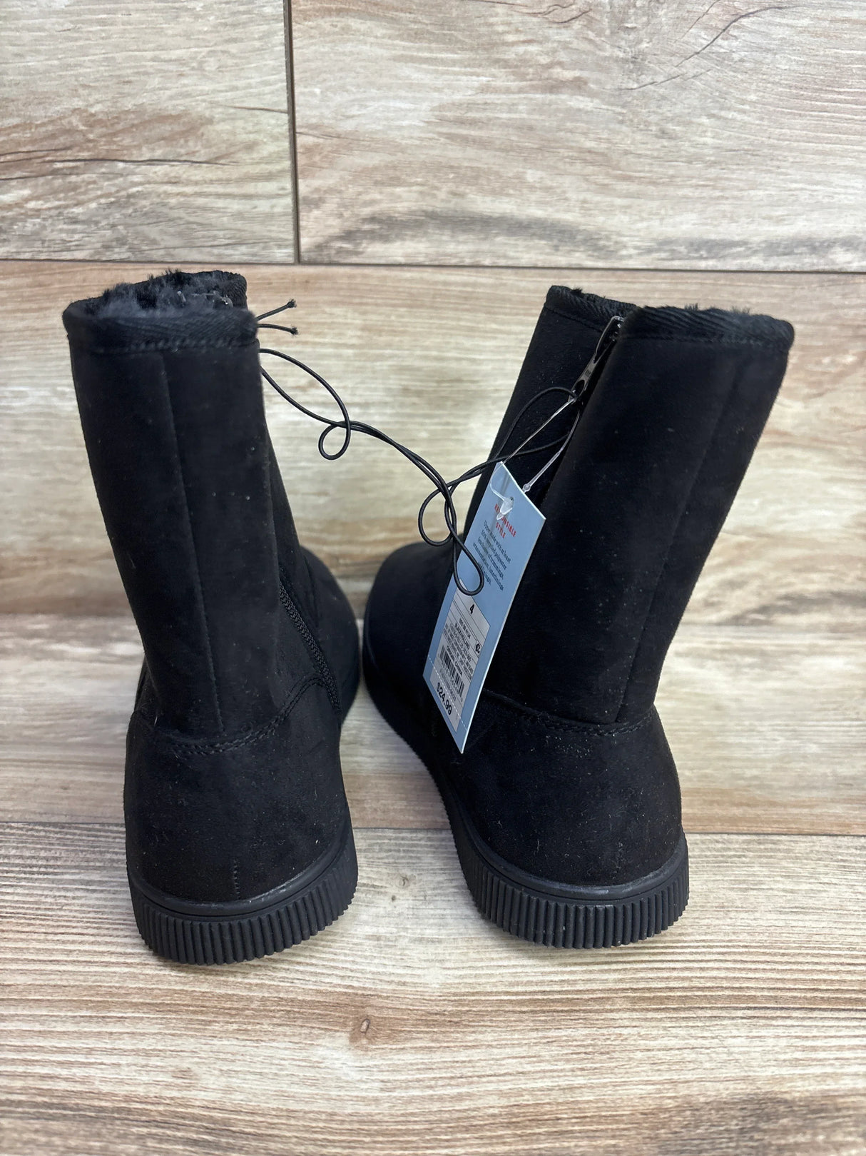 Pair of black suede kids boots with fur lining and price tag, displayed on wooden floor