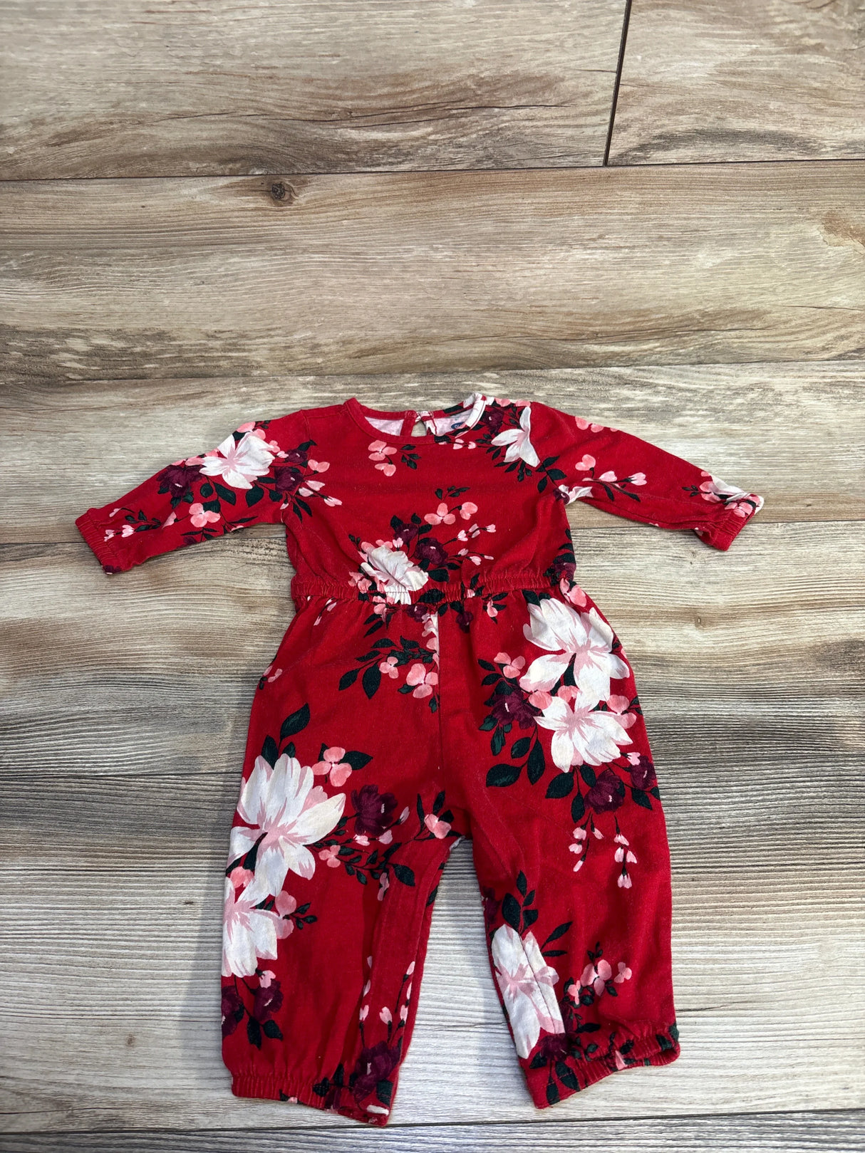 Red baby romper with long sleeves and floral print, laid flat on a wood floor