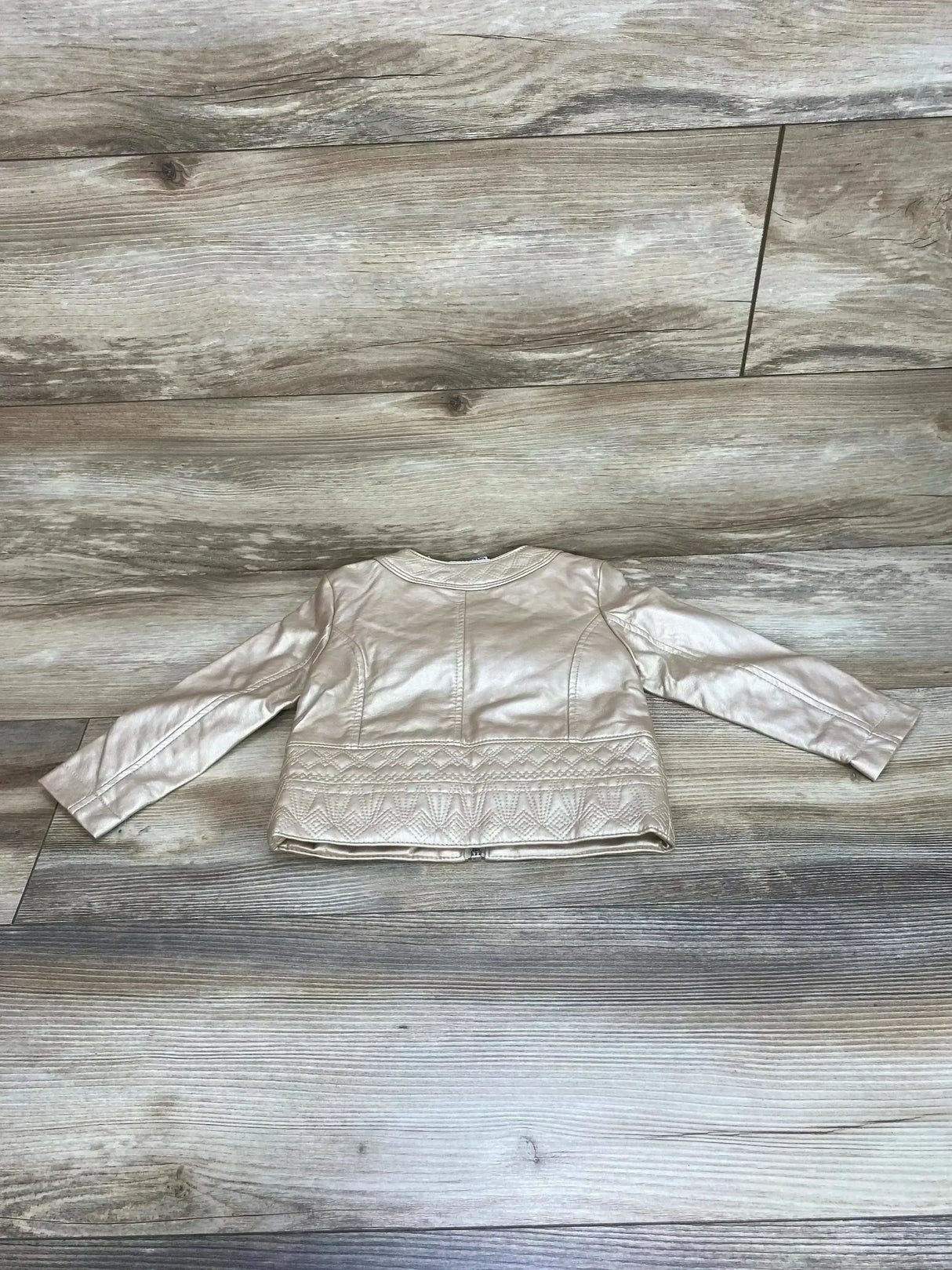Back view of Genuine Kids faux leather jacket, champagne (18m), showing quilted hem on wood background
