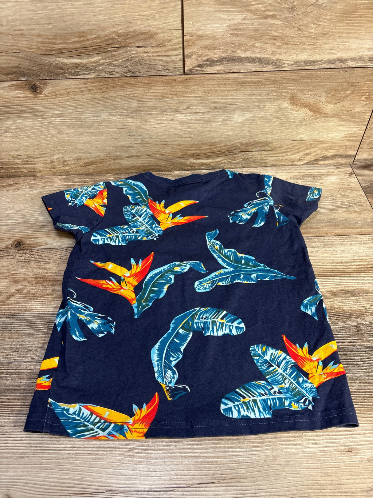 Navy blue toddler t-shirt with bright tropical leaf and bird of paradise flower print on wooden floor