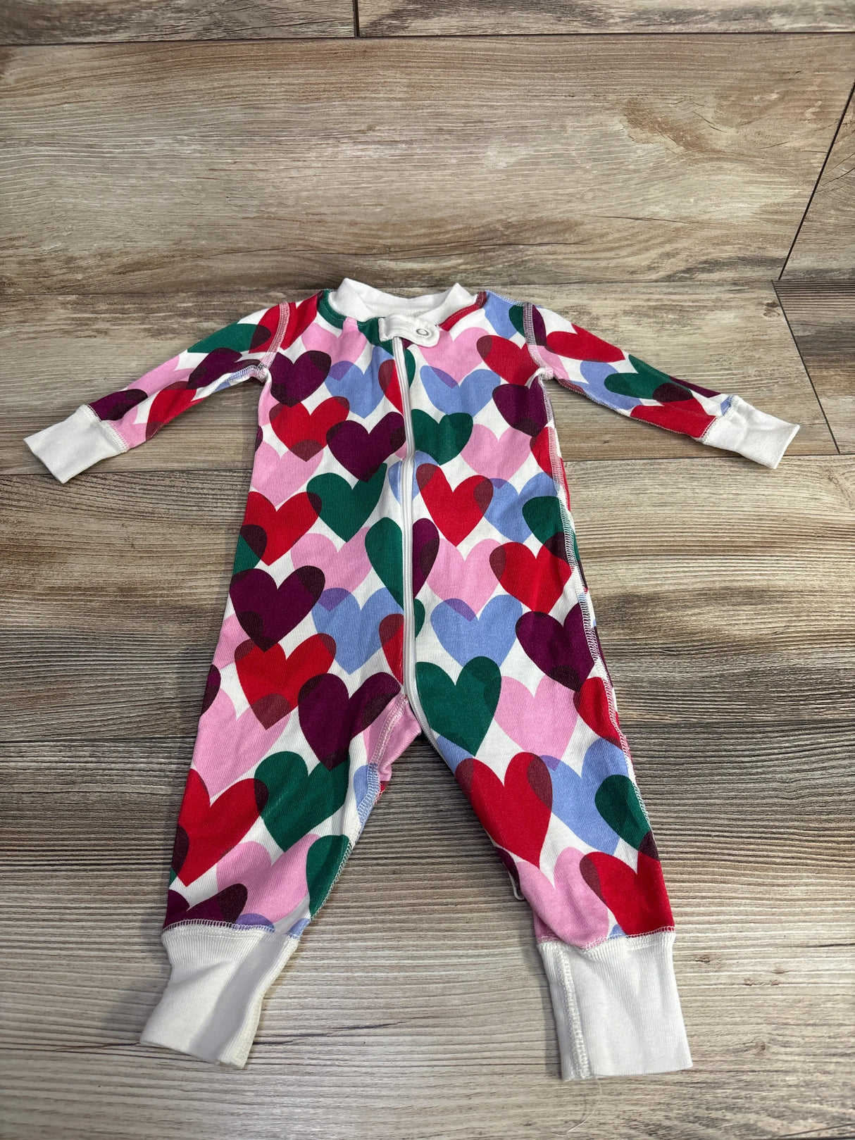 Colorful heart print baby sleeper with zipper, long sleeves, and white cuffs on wood floor