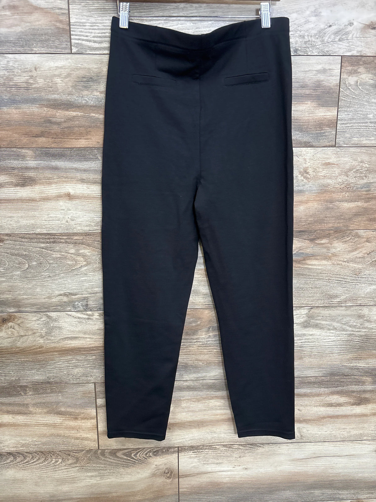 Front view of black maternity ankle pants showing tapered leg, pull-on high-rise panel and faux welt pockets on wood background