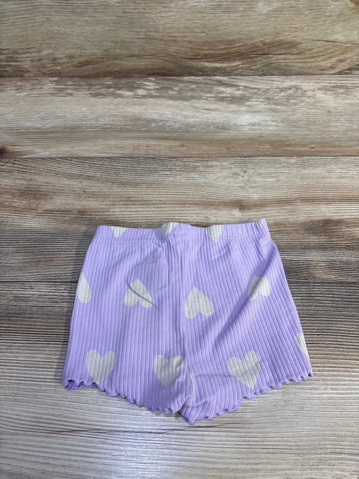 Flat lay of toddler purple ribbed bike shorts with white hearts and scalloped hem on light wood background