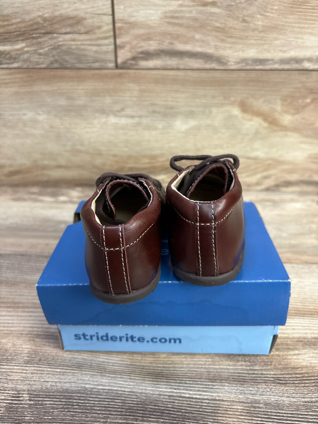 Rear view of Stride Rite SRTech Elliot sneakers, brown leather with white stitching, on blue shoebox on wood floor