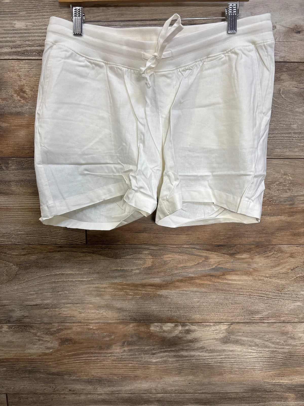 Front view of white Gap linen blend maternity shorts with under belly elastic waist, drawcord, and front pockets on wood floor