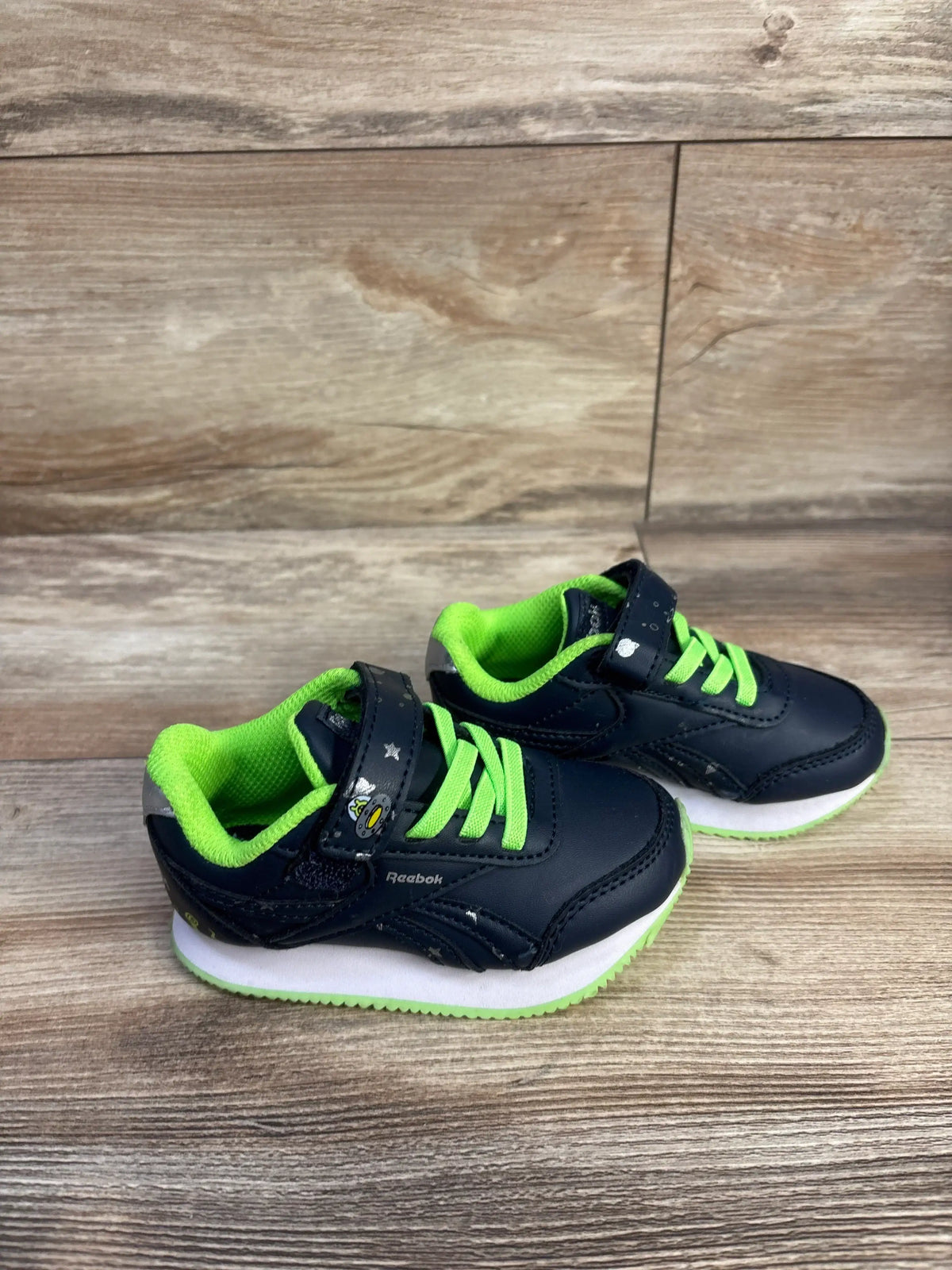 Three quarter view of Reebok Space Sneakers showcasing navy and green colors with hook and loop closure on a wood look floor