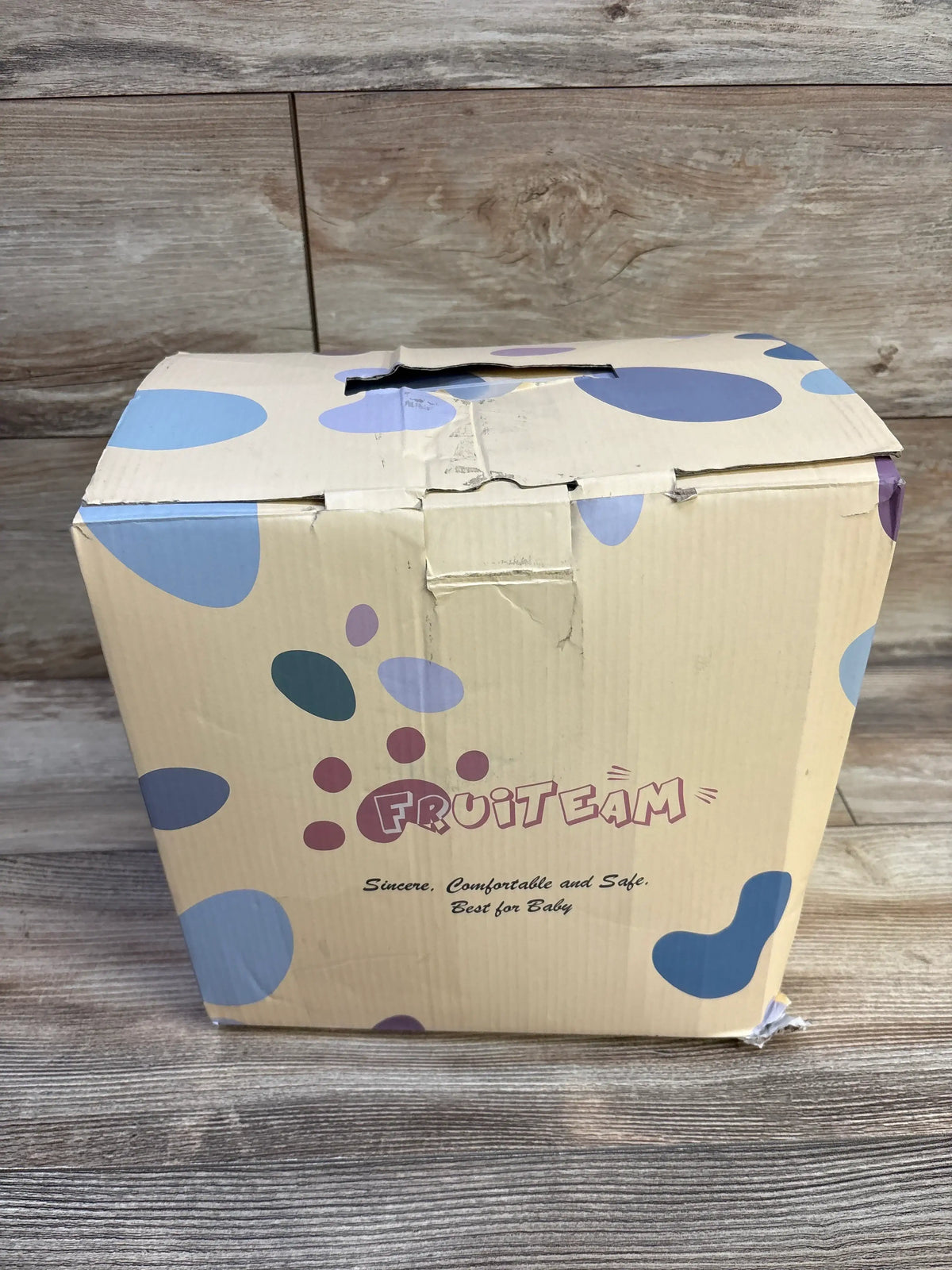 Packaging box for a FRUITEAM baby carrier with blue and purple circular patterns.