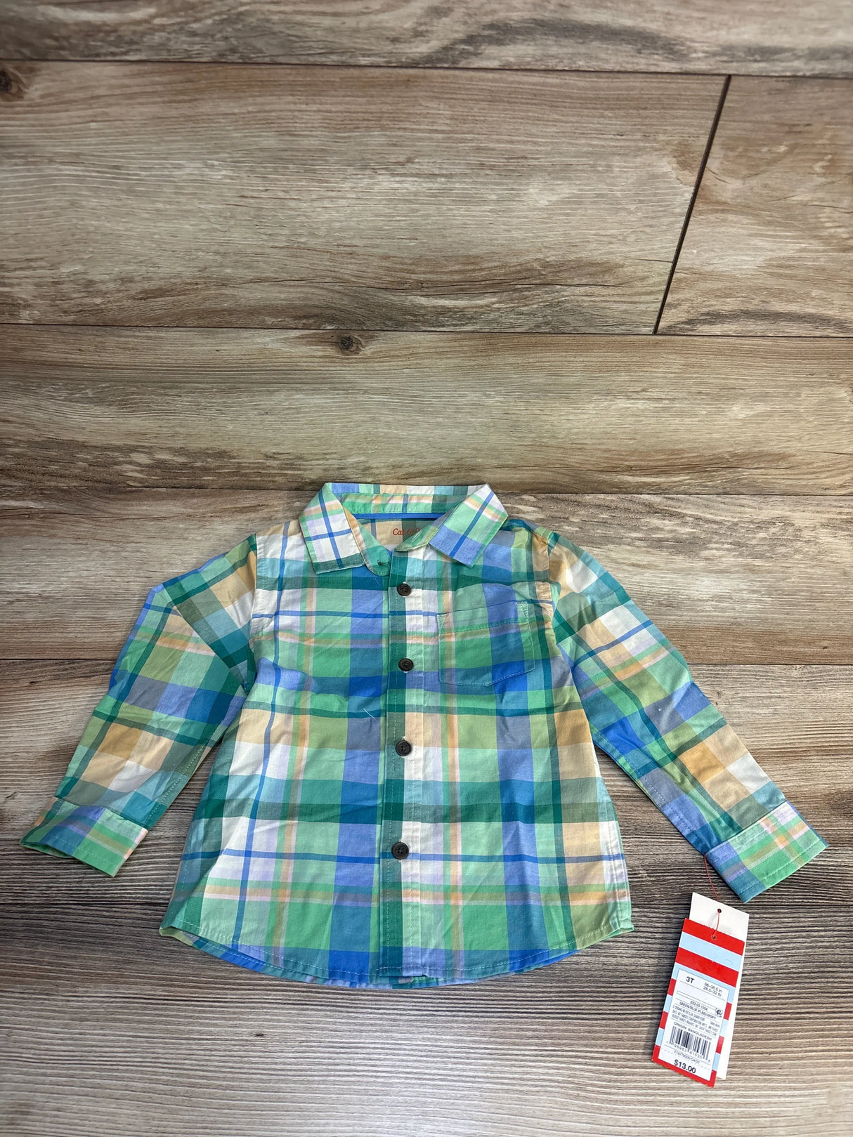 Green and blue plaid toddler shirt with buttons, laid on wooden floor, size 3T tag visible