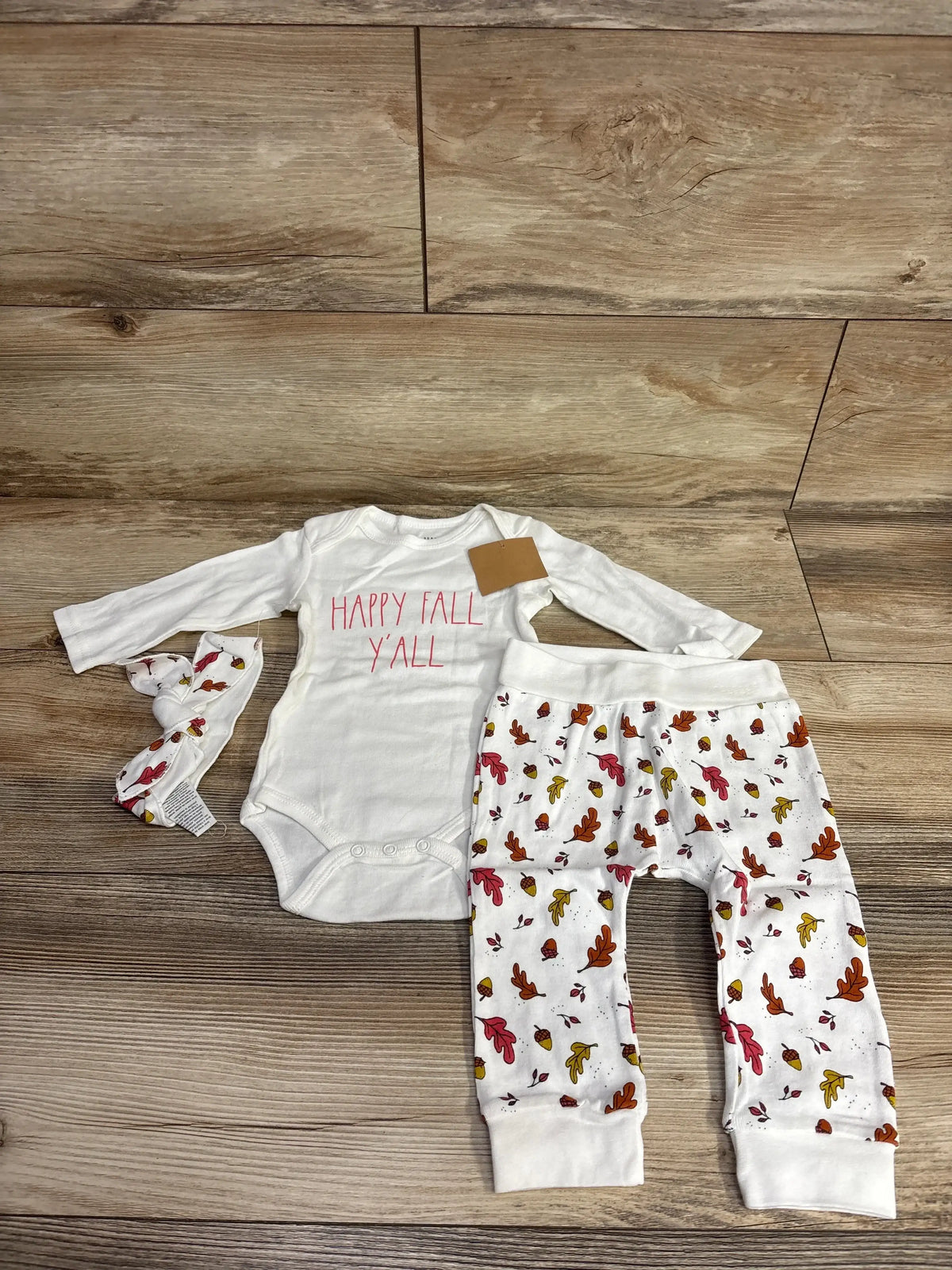 Baby fall outfit with 'Happy Fall Y'all' onesie, leaf-print pants, and matching headband on wood floor