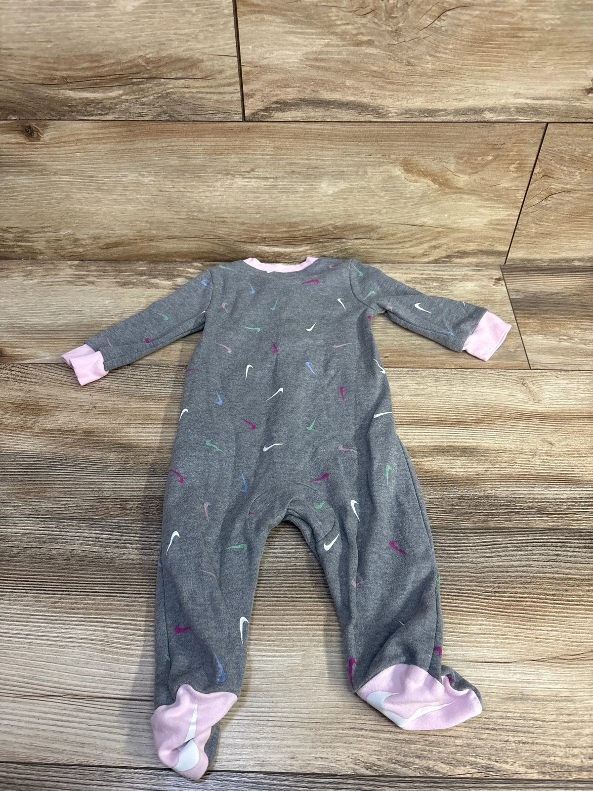 Front view of Nike gray snap sleeper, size 6 months, with multicolor swoosh pattern and pink cuffs on a wood floor