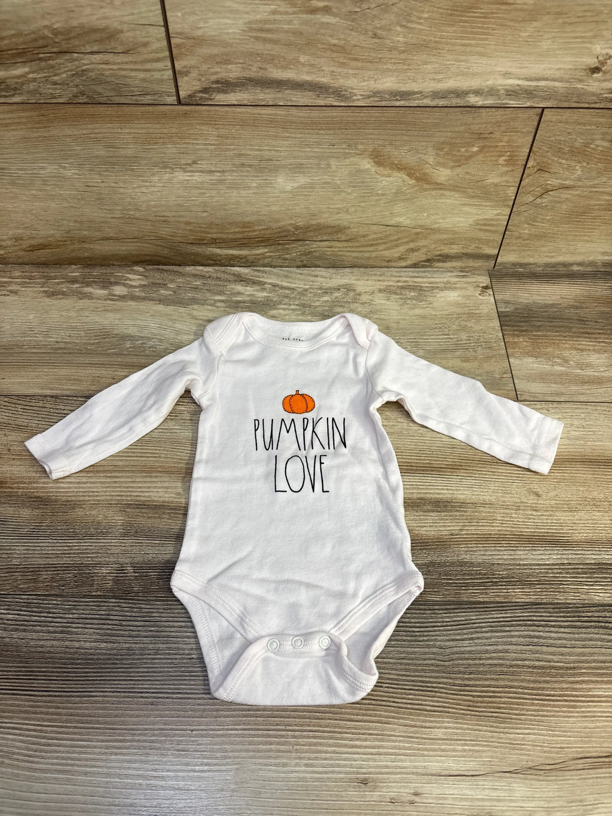 Front view of Rae Dunn pink Pumpkin Love bodysuit showcasing long sleeves and three snap closure on a wood look floor