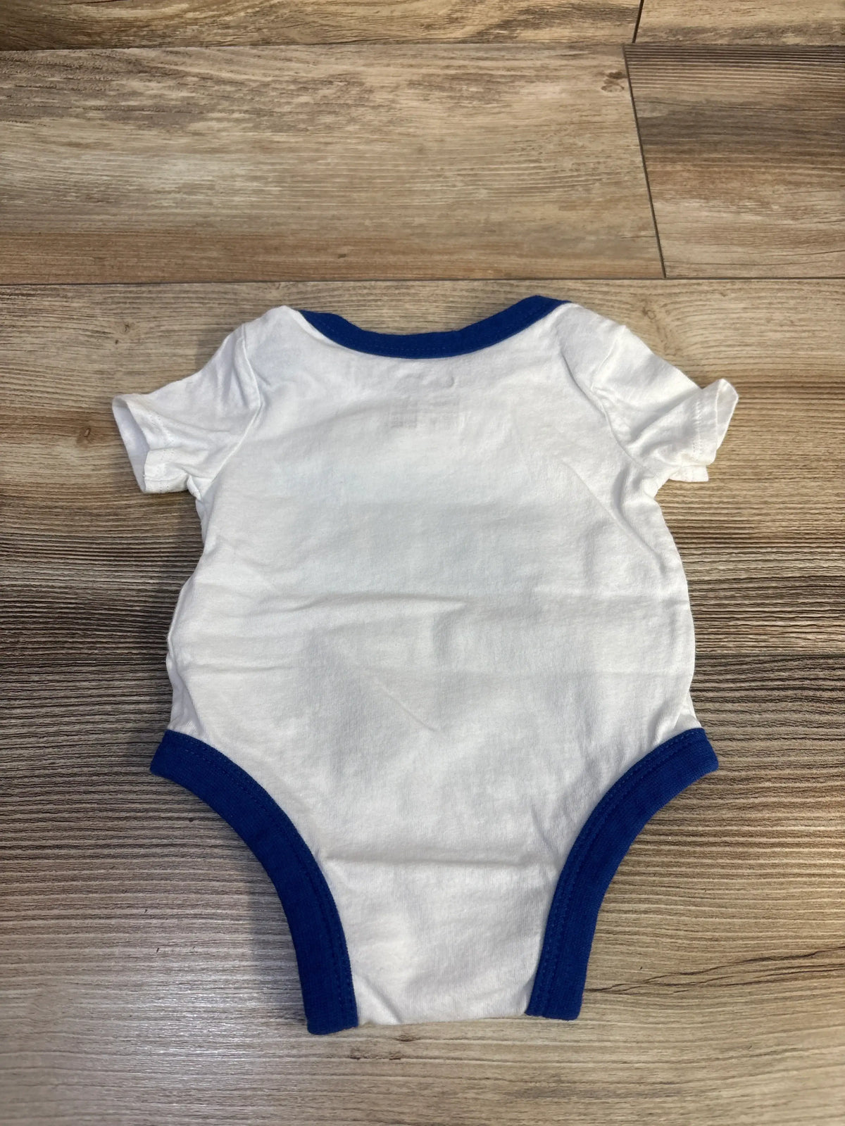 Flat lay of newborn white Nike bodysuit showcasing blue ribbed trim and short sleeves on wood floor