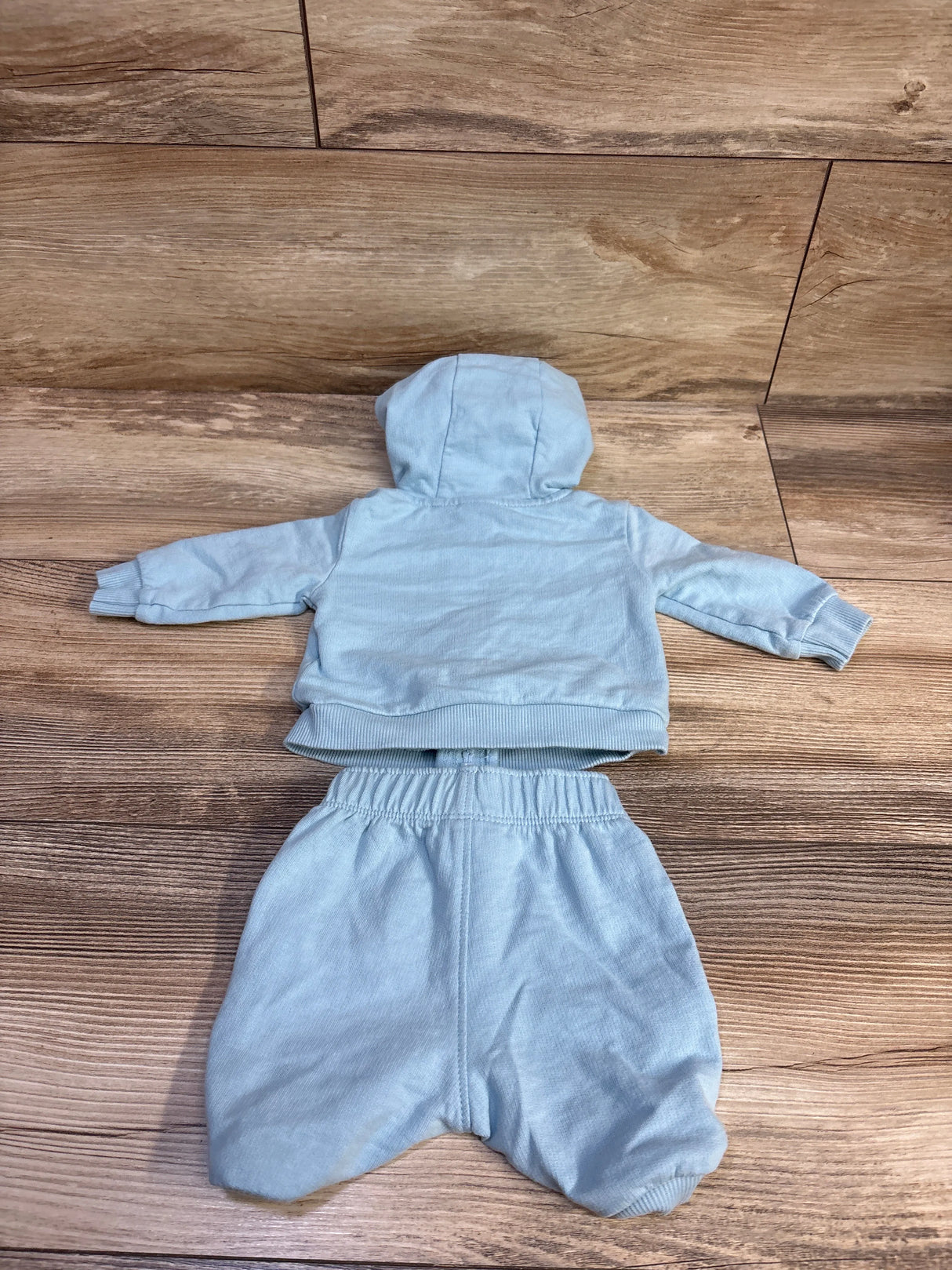 Back view of Carter’s newborn blue zip-up hoodie and matching pants showing hood, ribbed cuffs, and elastic waistband on wood background
