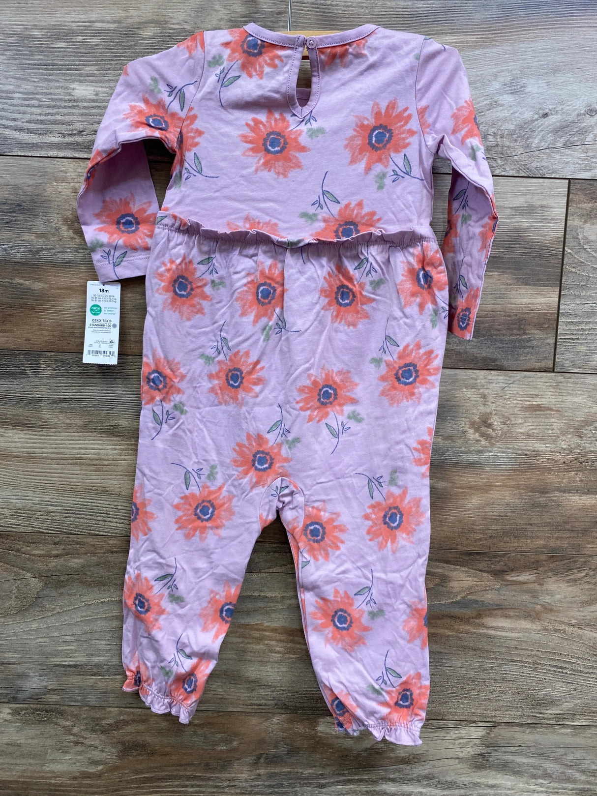 Purple long-sleeve baby romper with orange floral print and ruffled ankles laid on wooden floor