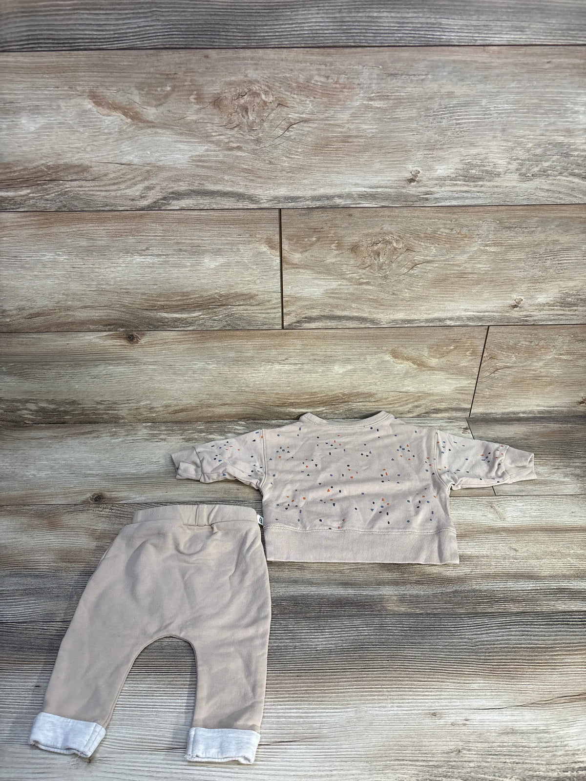 Overhead view of Easy Peasy organic long sleeve shirt and pants set showcasing beige pants and patterned shirt on a wood surface