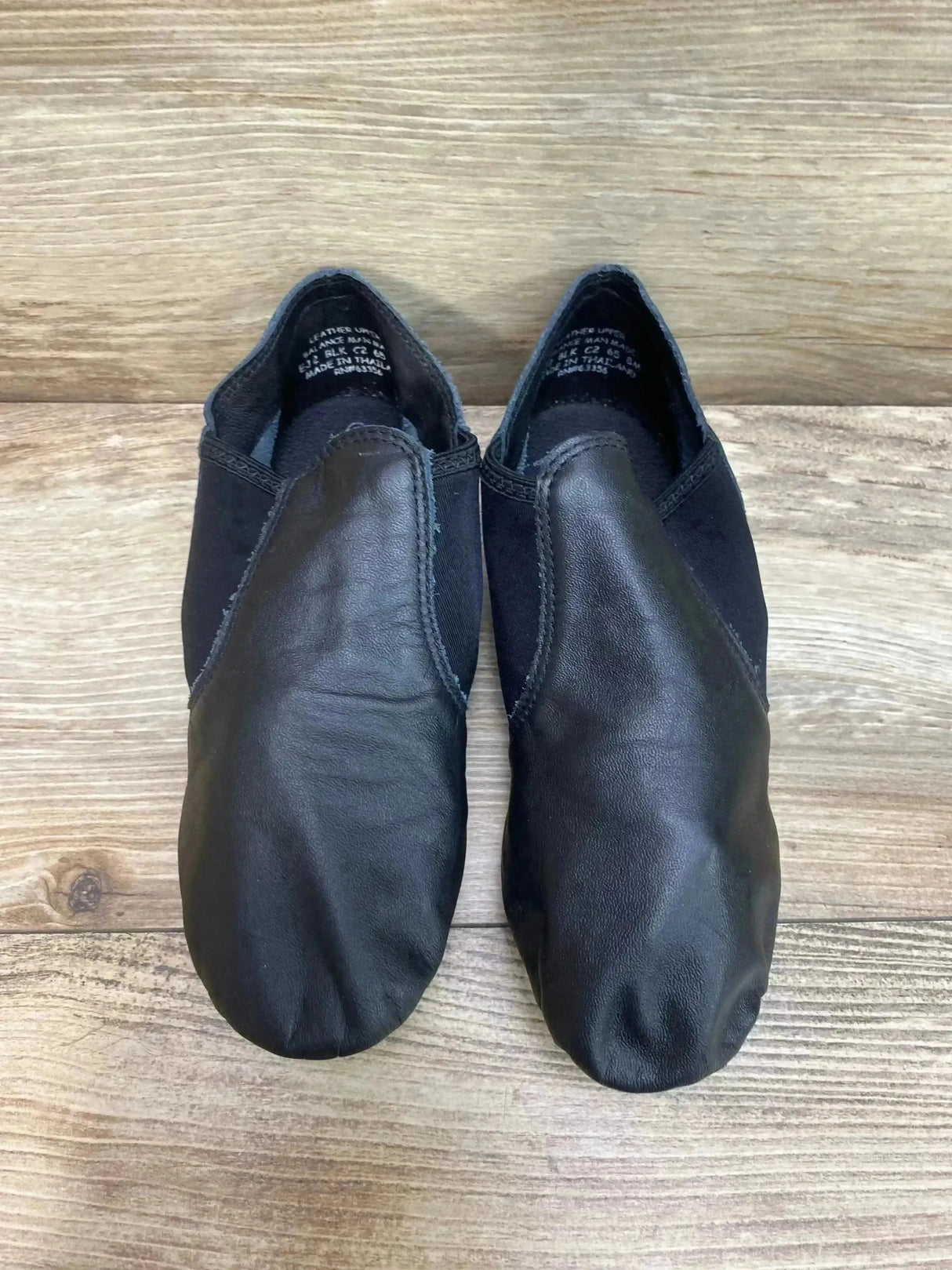 Top view of Capezio E-Series black jazz slip-on shoes size 8C showing leather vamp and elastic side panels on wood floor
