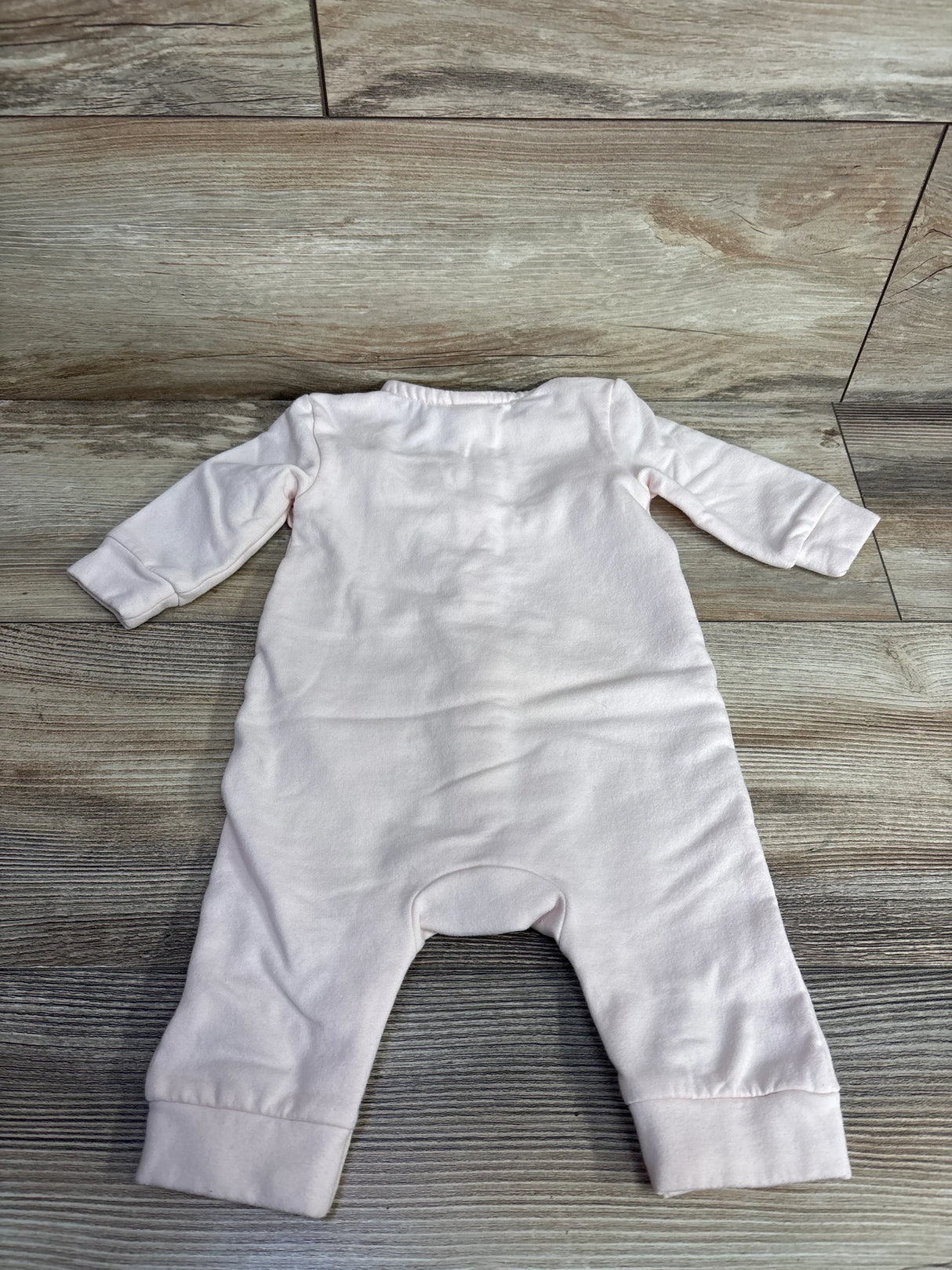 Light pink long sleeve baby romper laid flat on wood floor, children's clothing resale