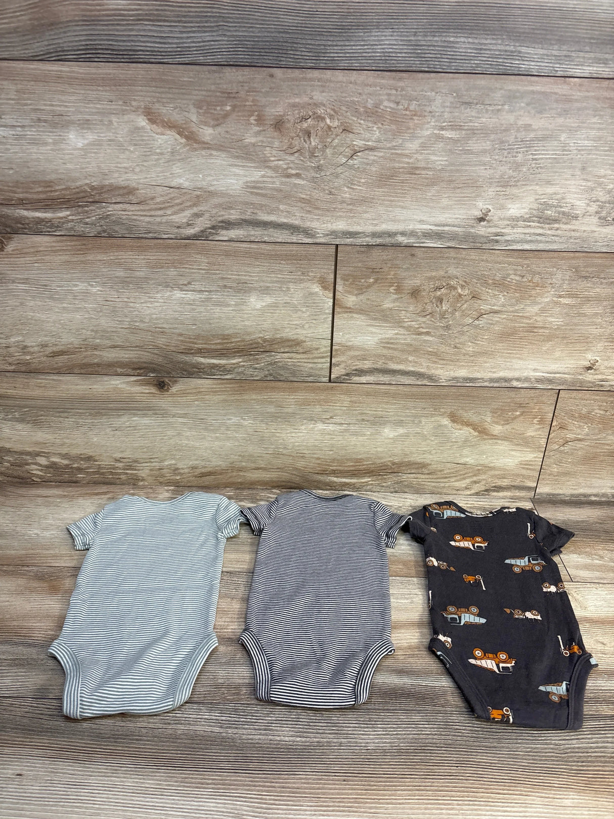 Flat lay of Carter's three pack bodysuit set showcasing grey striped solid grey and navy animal print short sleeve bodysuits on wood plank floor