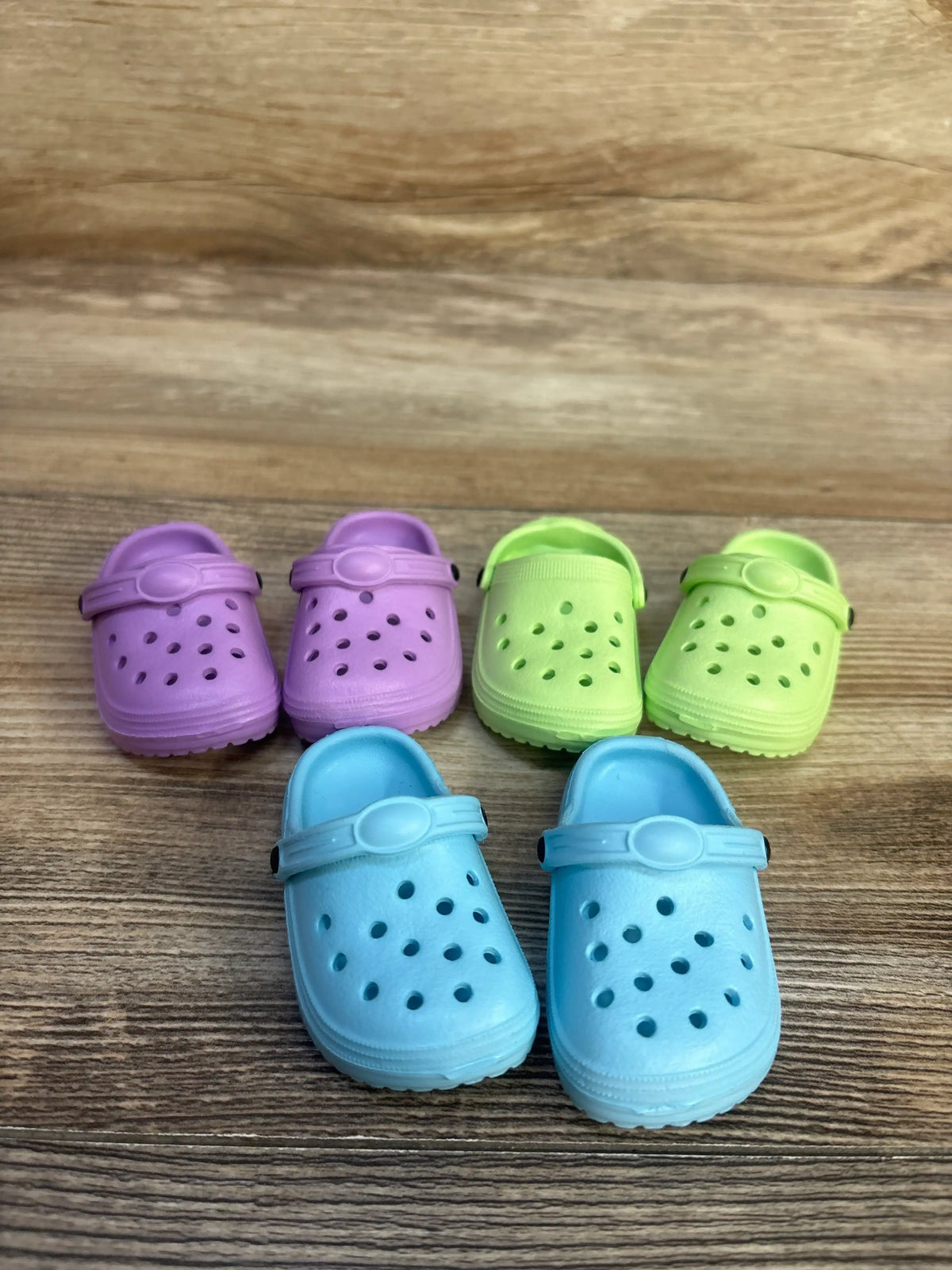 Top view of HXIELEC 3pk clog shoes for dolls showcasing purple, green, and blue pairs on a wood-grain surface