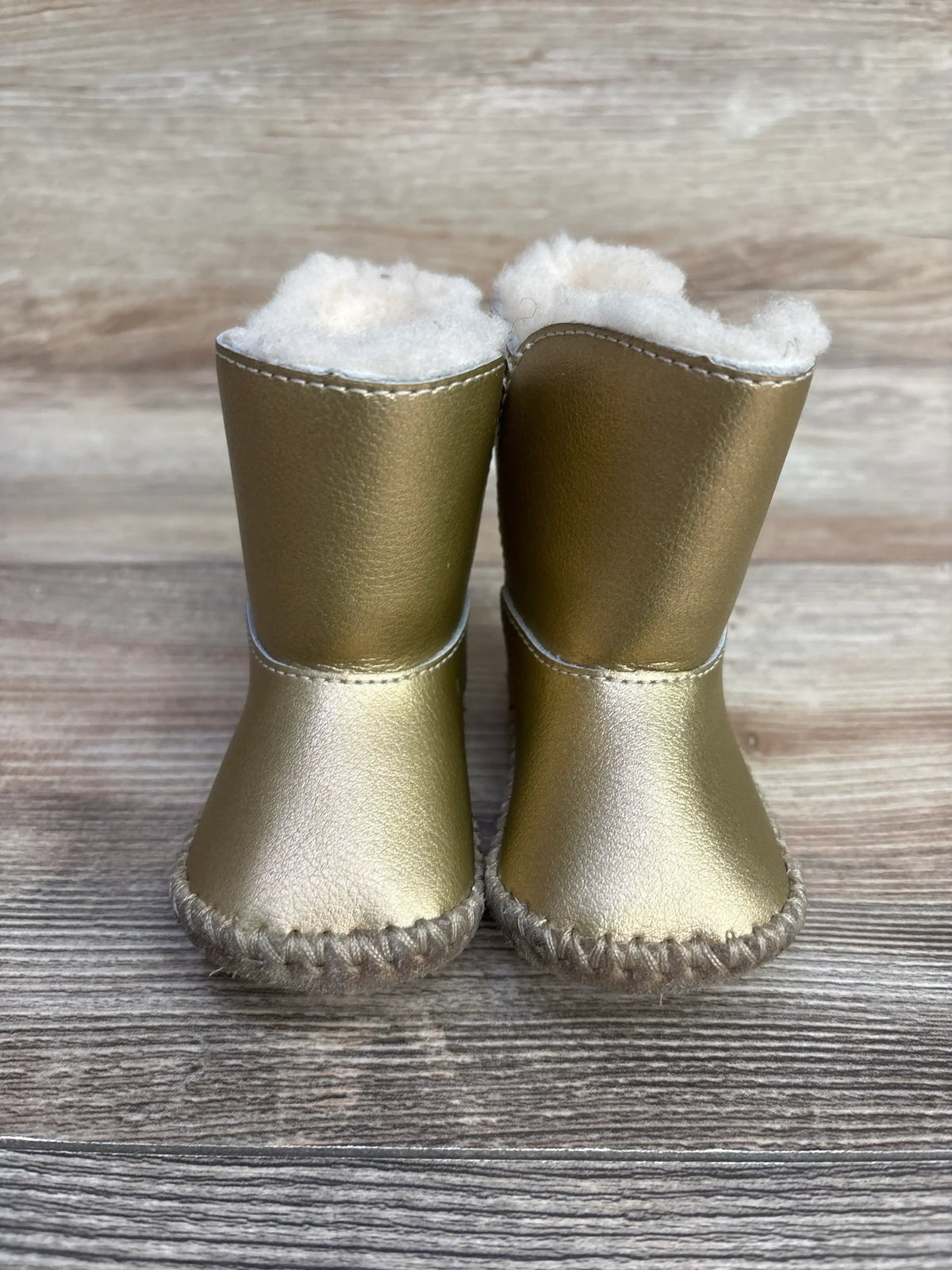 Pair of small gold baby boots with white fluffy lining on wooden surface