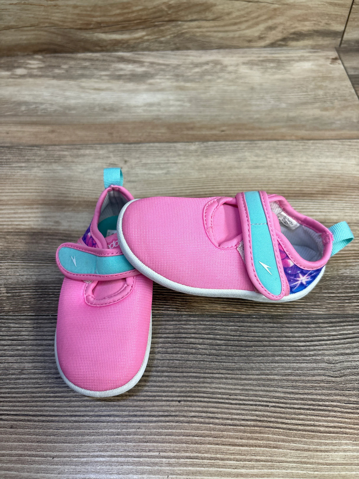 Front view of Speedo Shore Explorer toddler water shoes, pink upper with aqua strap and pull tab, white sole on wood