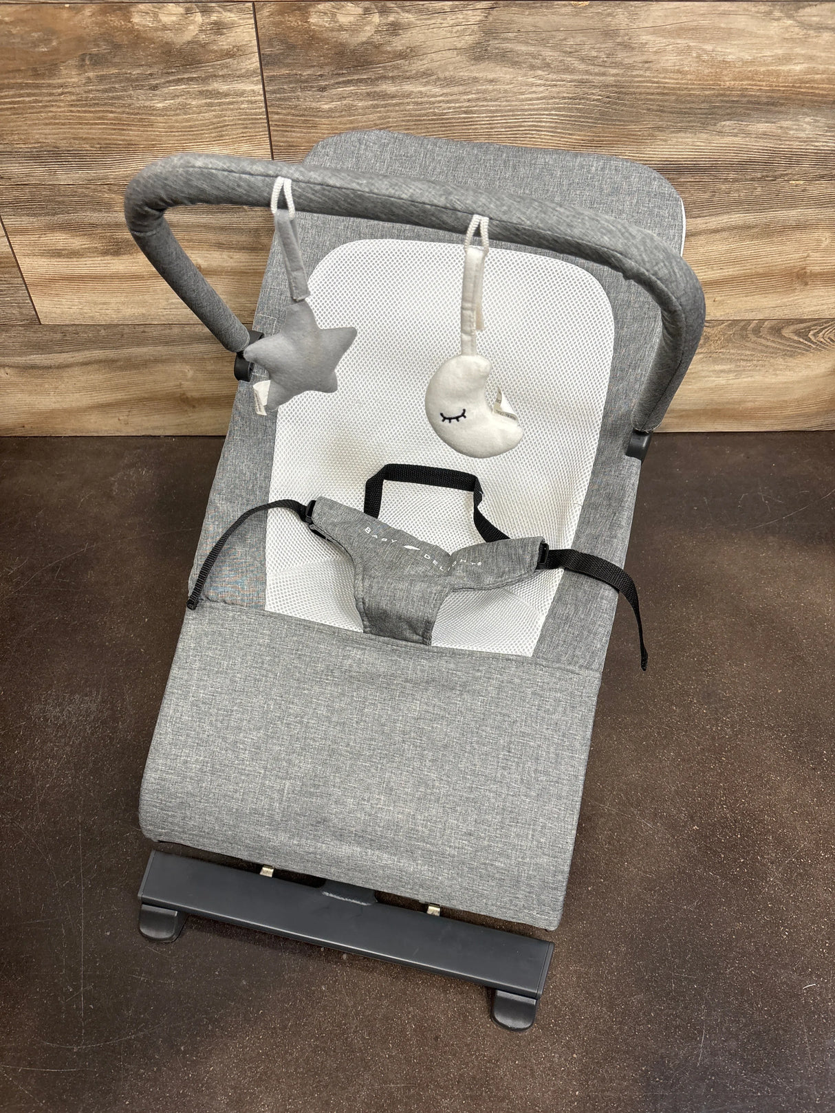 Top view of Baby Delight Alpine Deluxe Bouncer in Charcoal Grey showing mesh seat and toy bar with star and moon on wood floor