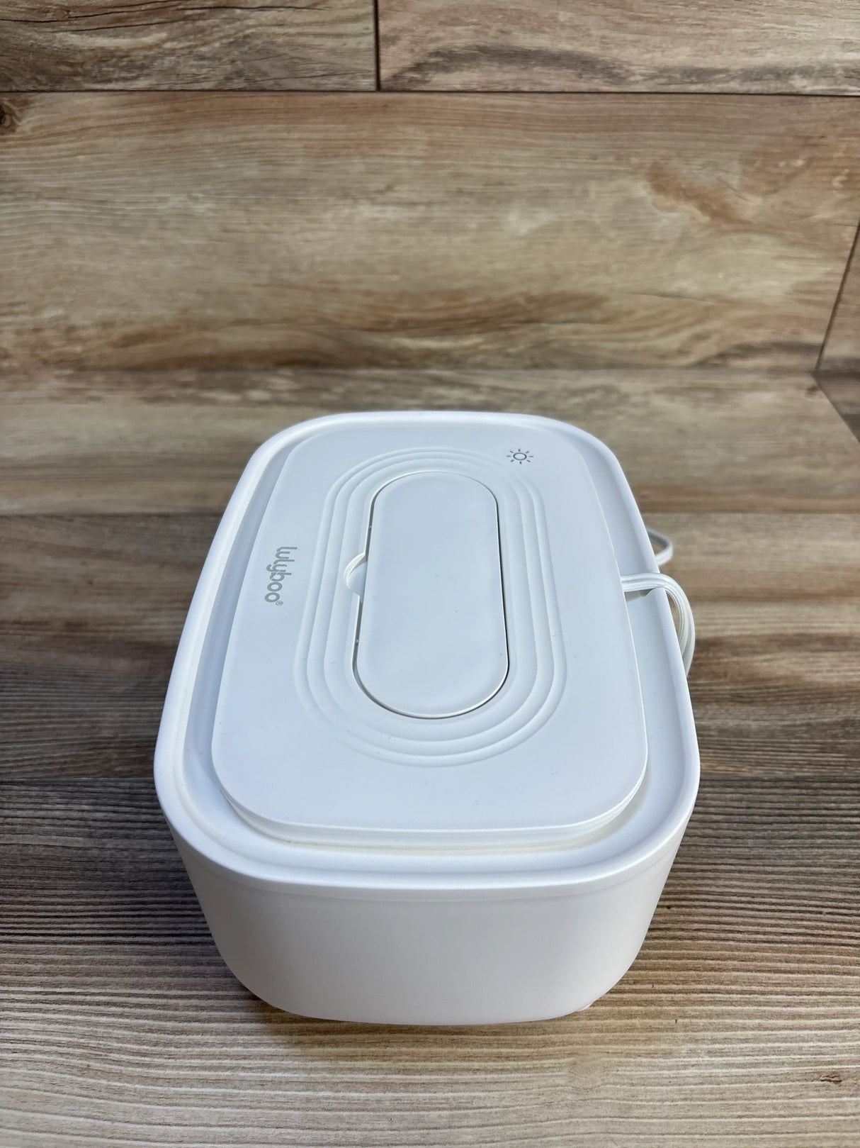 Three-quarter view of Lulyboo Wipe Warmer and Dispenser, White showcasing its lid, indicator light, and power cord on a wood surface