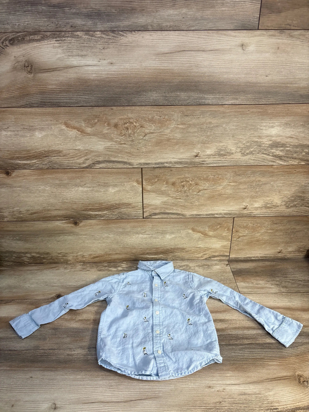Front view of Janie & Jack blue linen-cotton button-up shirt showcasing embroidered bird icons with a wood background