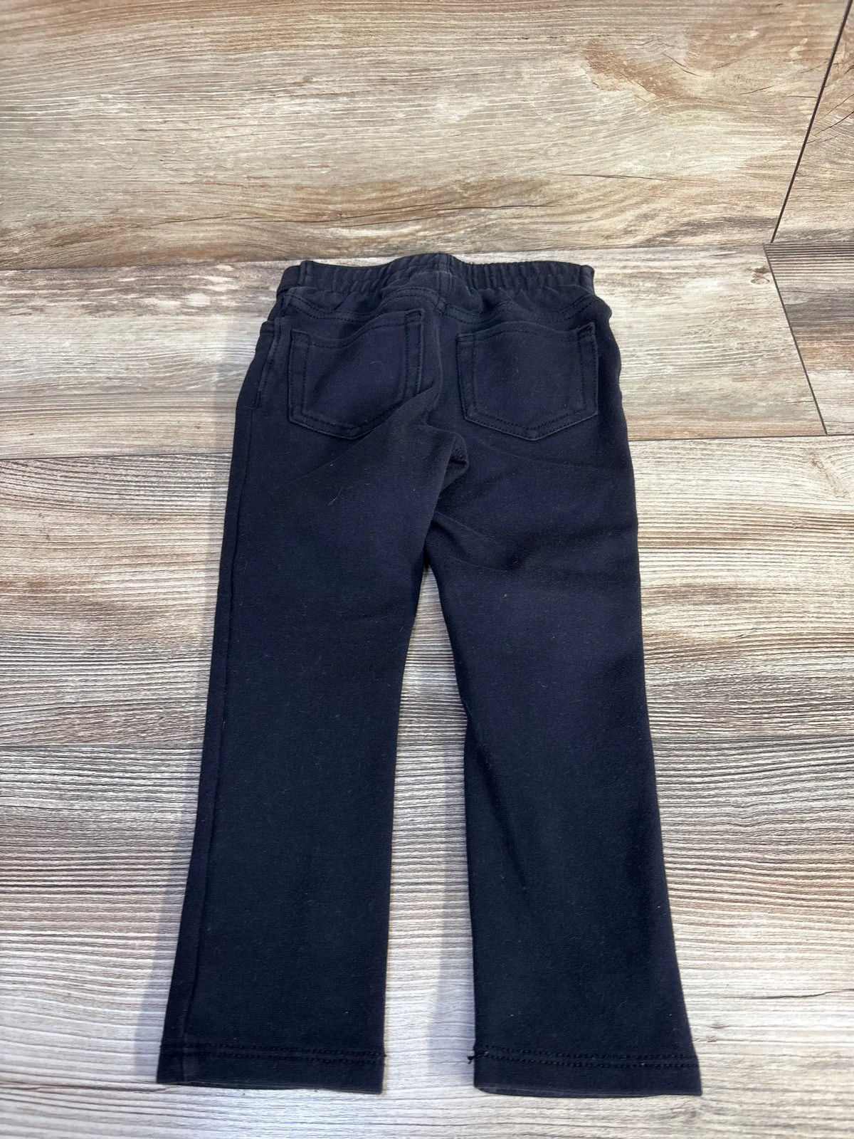 Rear view of Children’s Place black pants showcasing elastic waistband and two back pockets on a wood-patterned floor