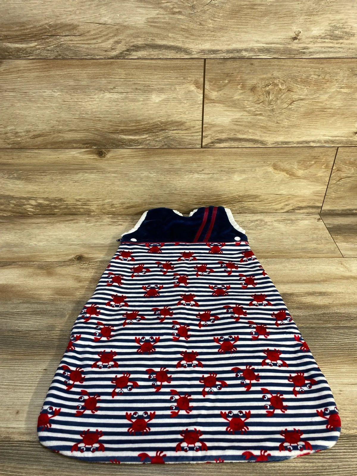 Top-down view of navy newborn sleep sack by Bumbershoots with red crab print on navy-and-white stripes and navy velour top