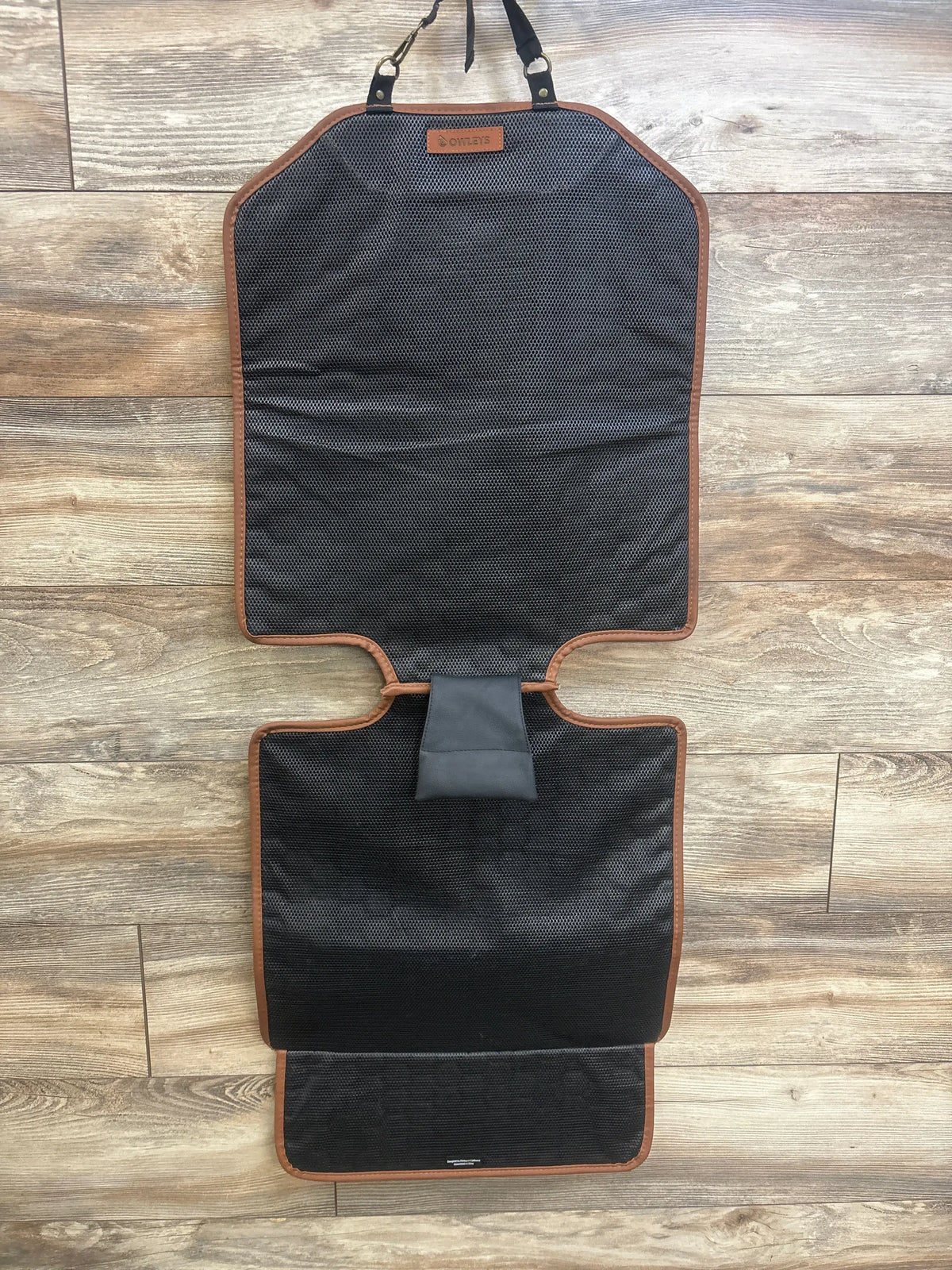 Front view of Owleys Premium Leather Car Seat Protector showcasing black padded sections and brown trim on wood flooring
