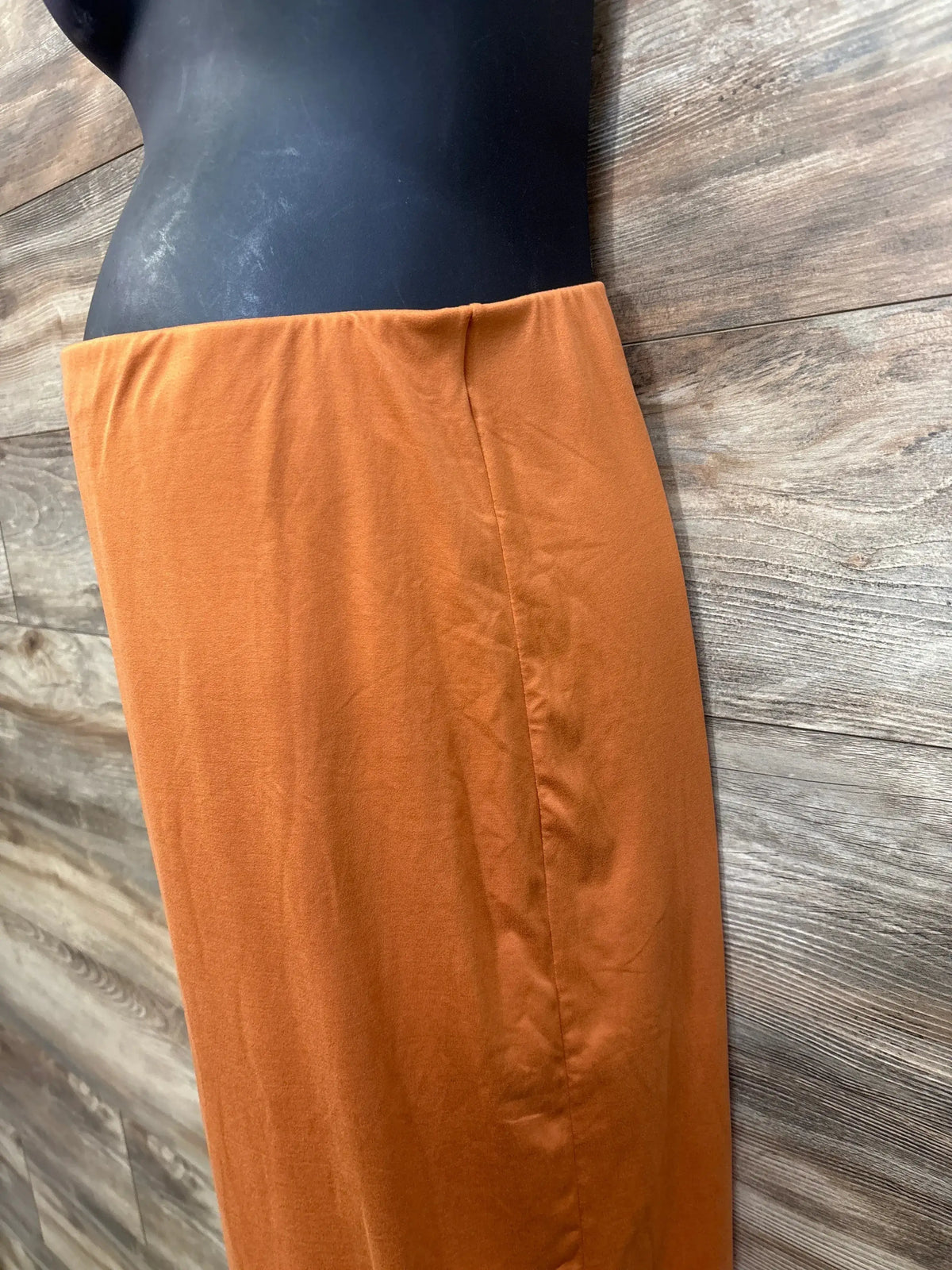 Side view of Poshdivah orange maternity skirt with fold over waistband and straight fit on black mannequin, wood background