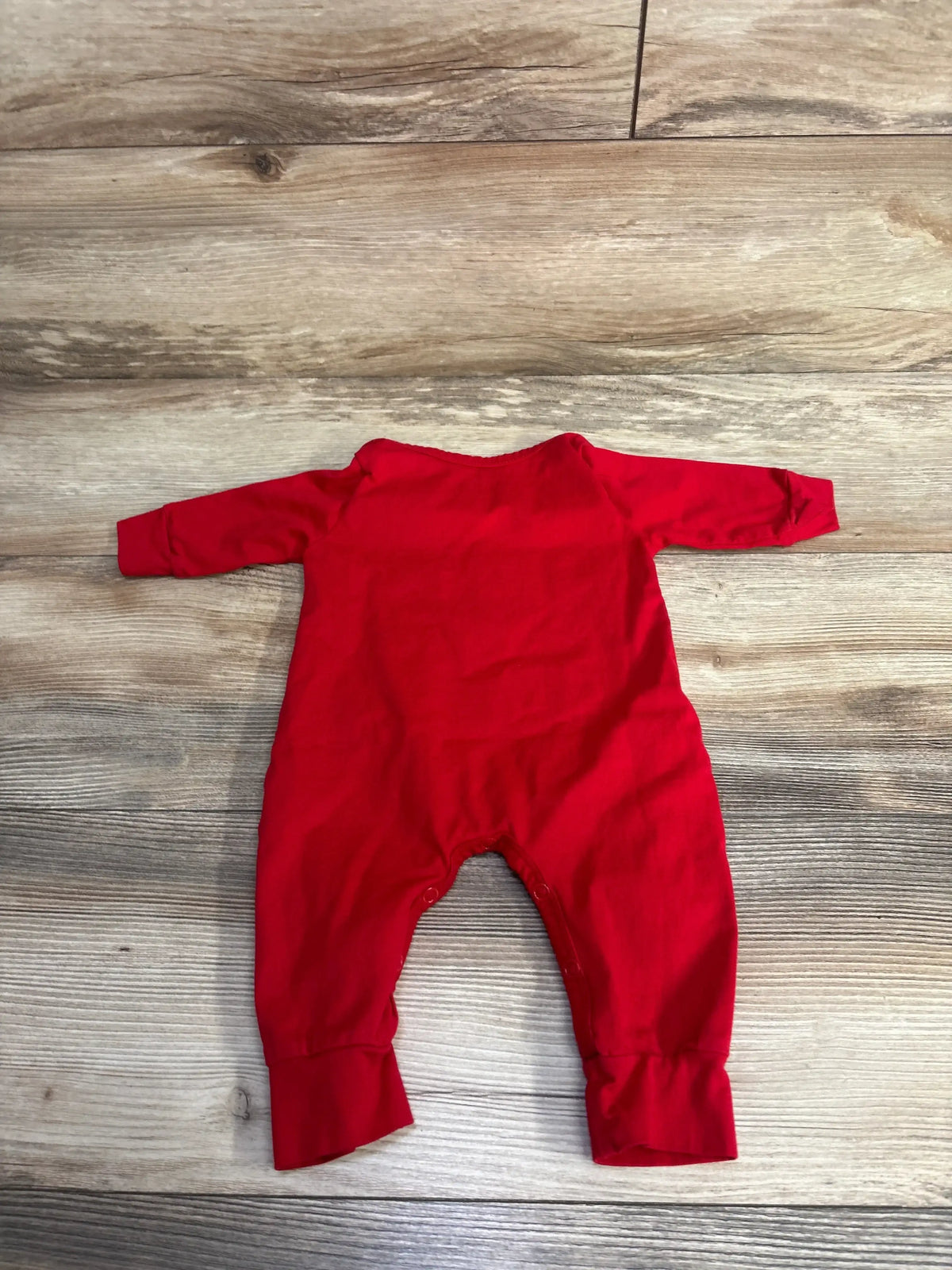 Red baby onesie with long sleeves and snap closures, laid flat on wood floor