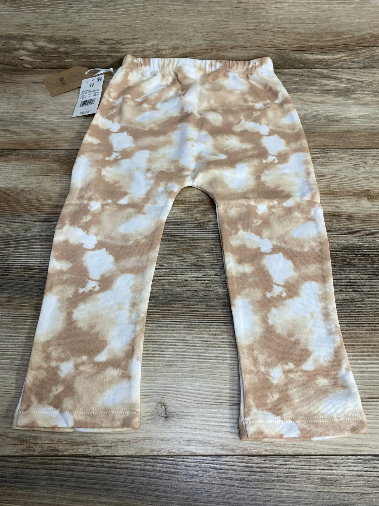 Flat lay of NEW Grayson Collective Tie Dye Pants showcasing brown and cream tie dye pull on pants with hangtag on wood plank floor