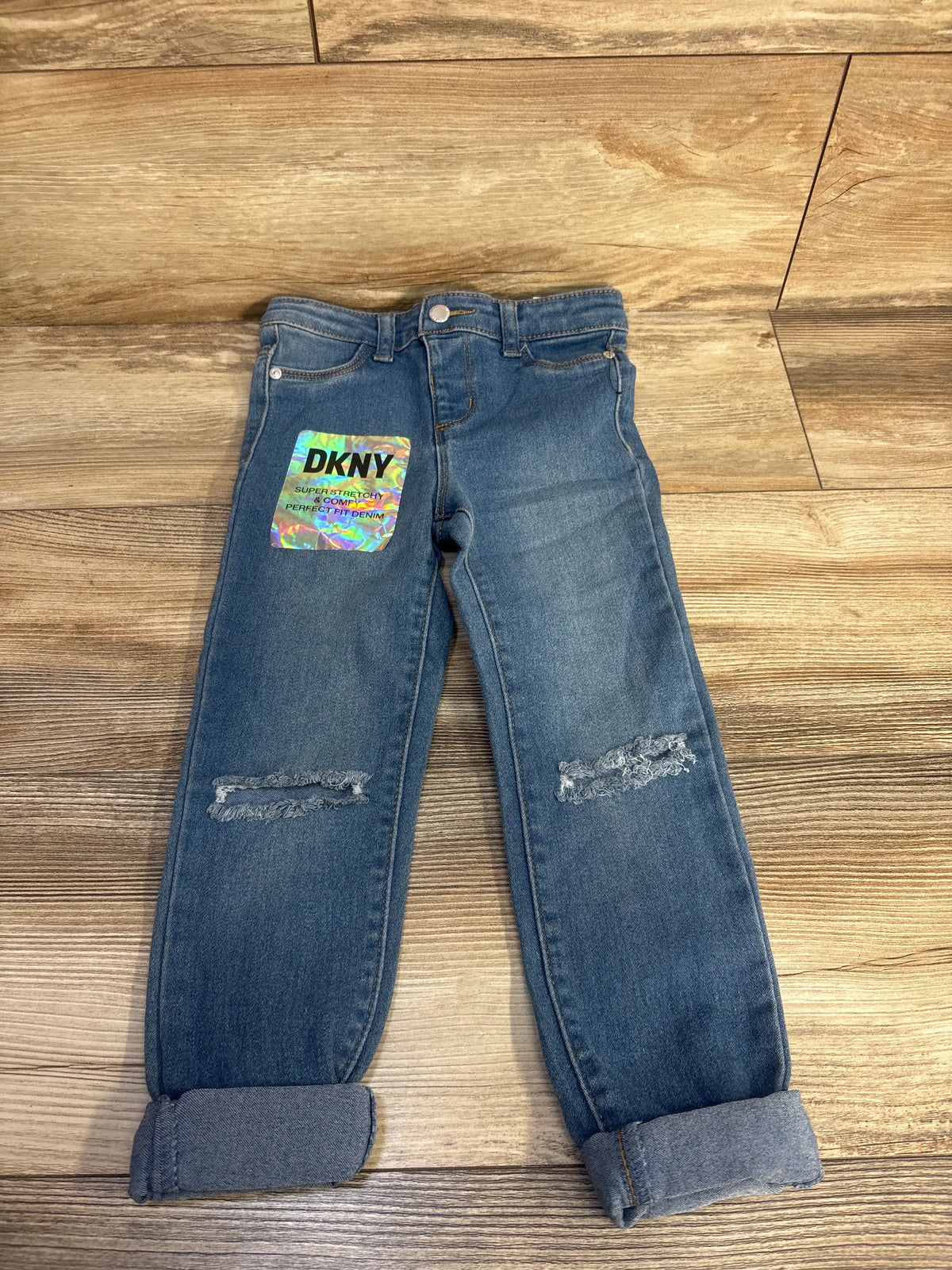 Front view of NEW DKNY distressed blue toddler jeans in size 5T showcasing knee distressing and cuffed hems on a wood floor