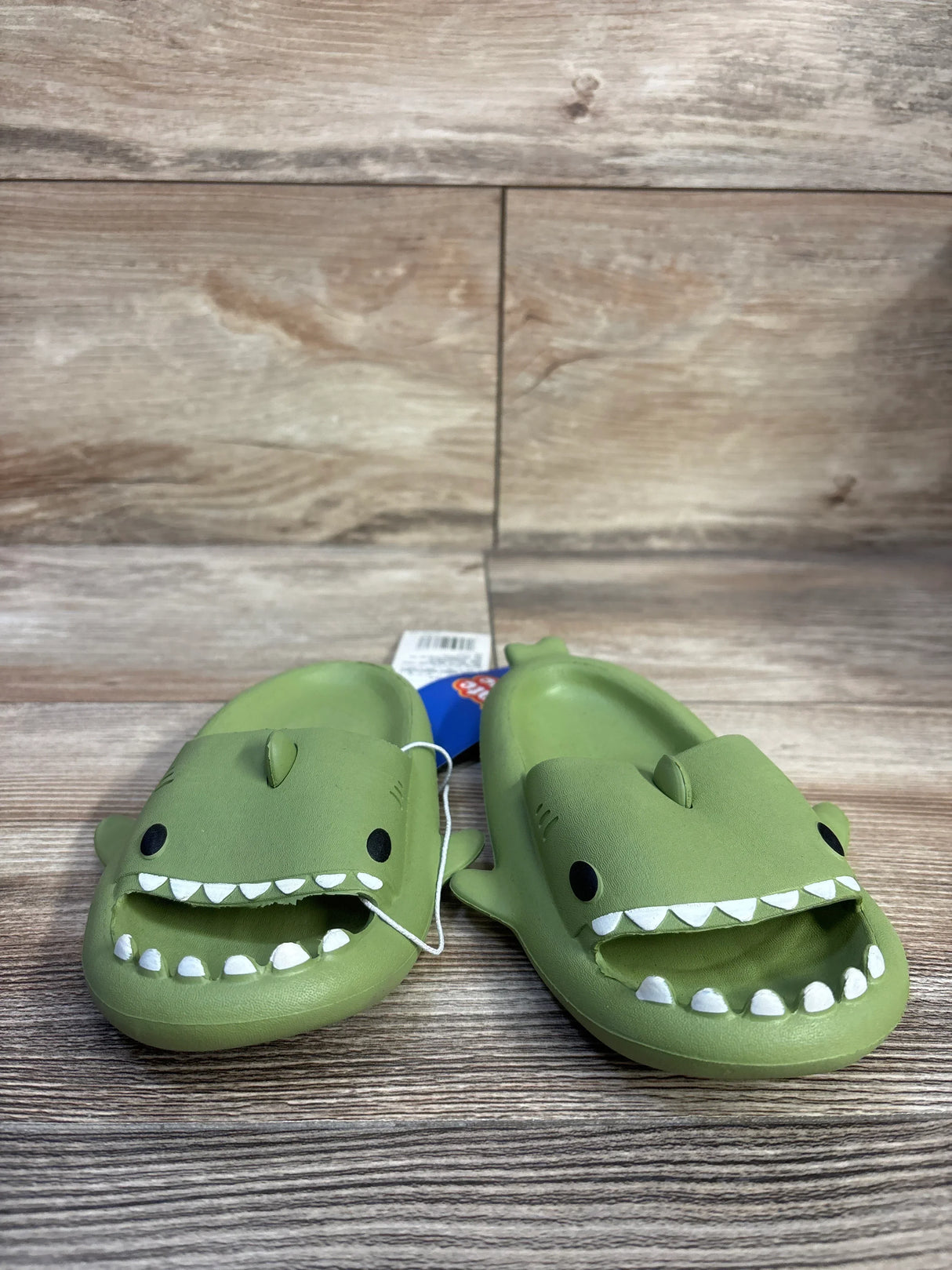 Front view of Crayon Friends shark slides showcasing green shark-face upper with white teeth and molded fin details on a wood plank background