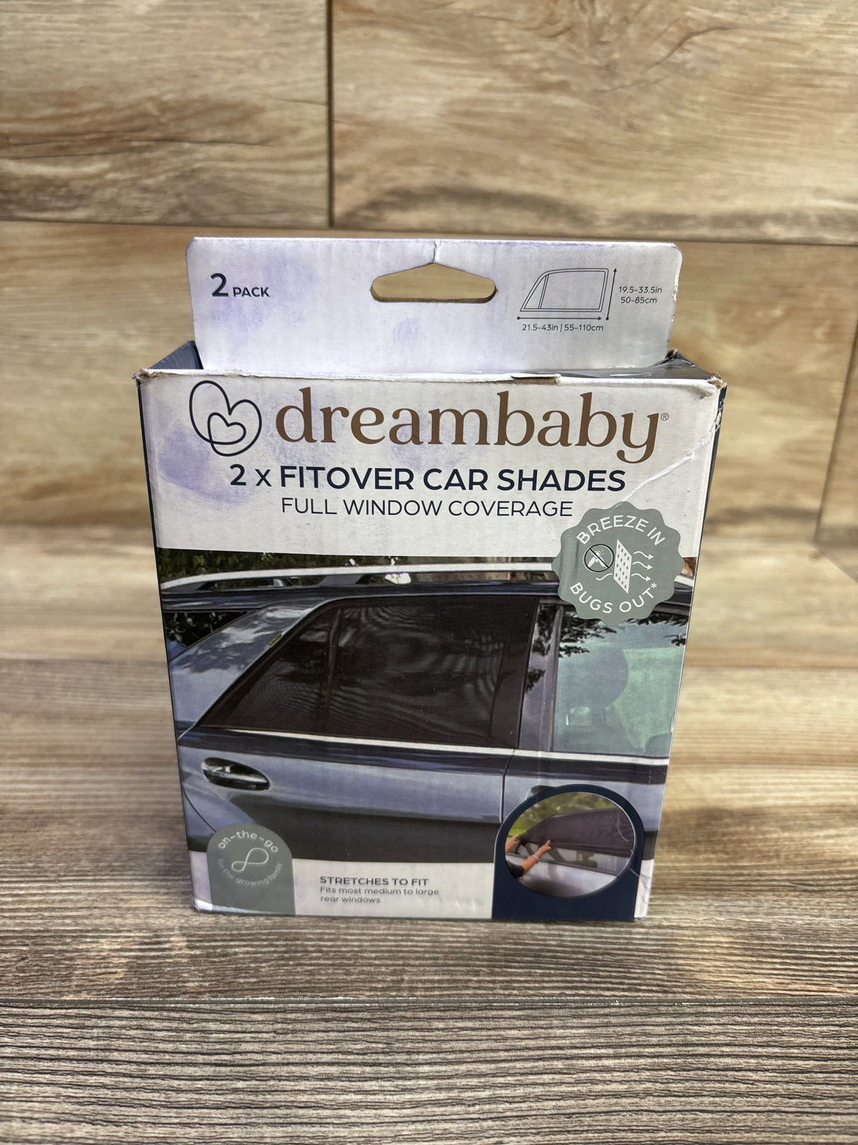 Front view of Dreambaby 2-pack Fit-Over Car Window Shades box showcasing a fitted shade on a car rear door window and the visible Full window coverage headline on a wood background