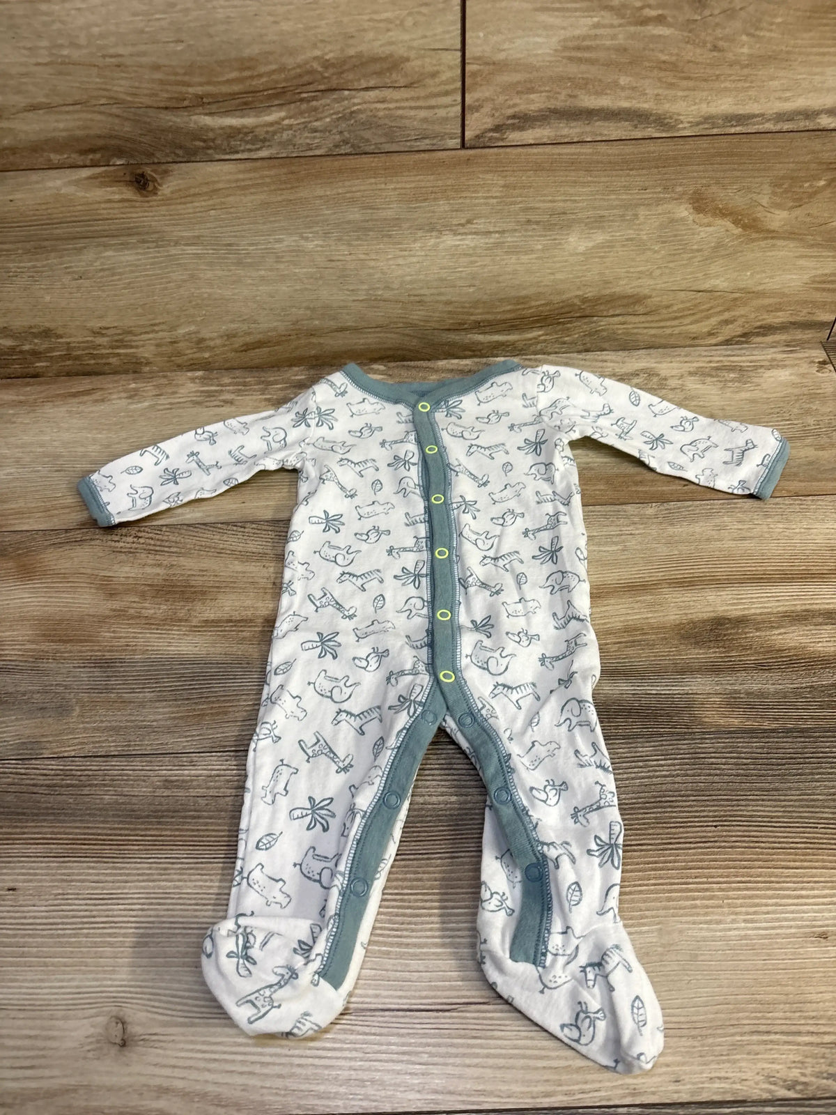 Flat-lay front view of white footed baby snap sleeper with teal trim and gray animal print on wood background