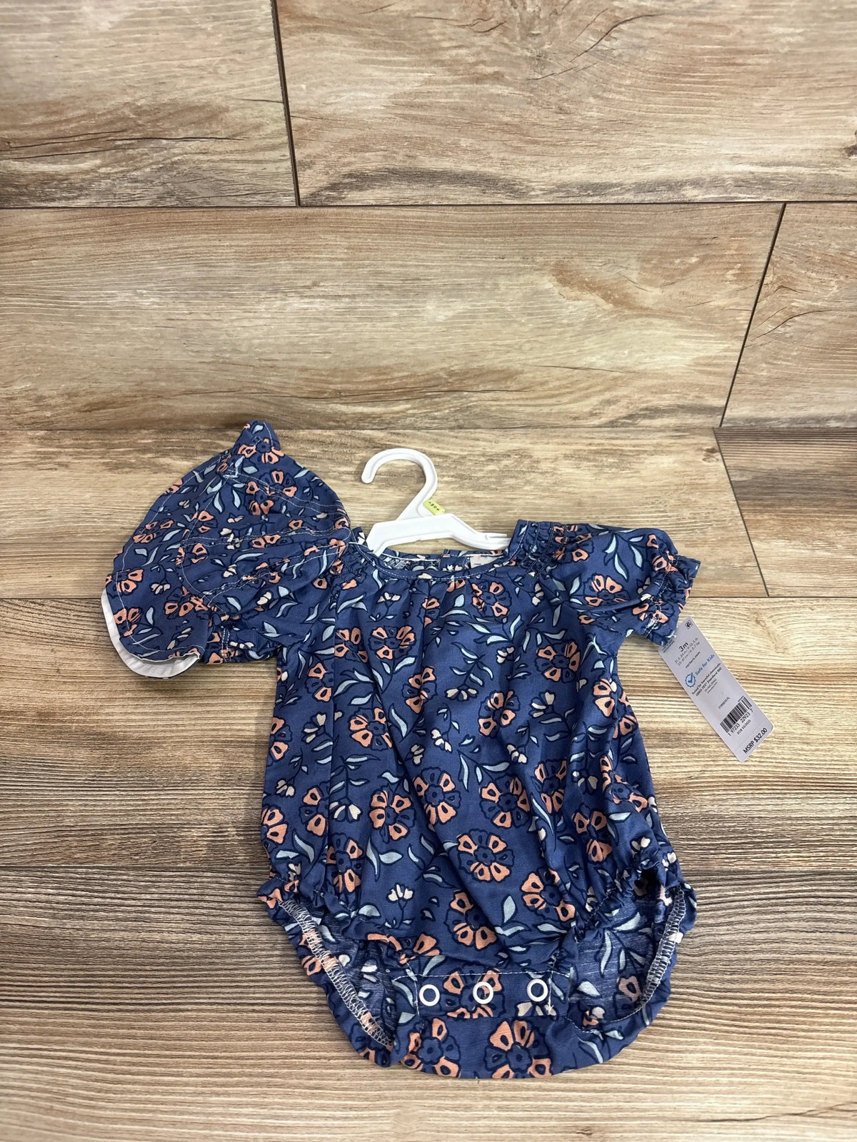 Top down view of blue floral baby bubble romper with matching bucket hat showing puff sleeves and snap crotch on wood surface