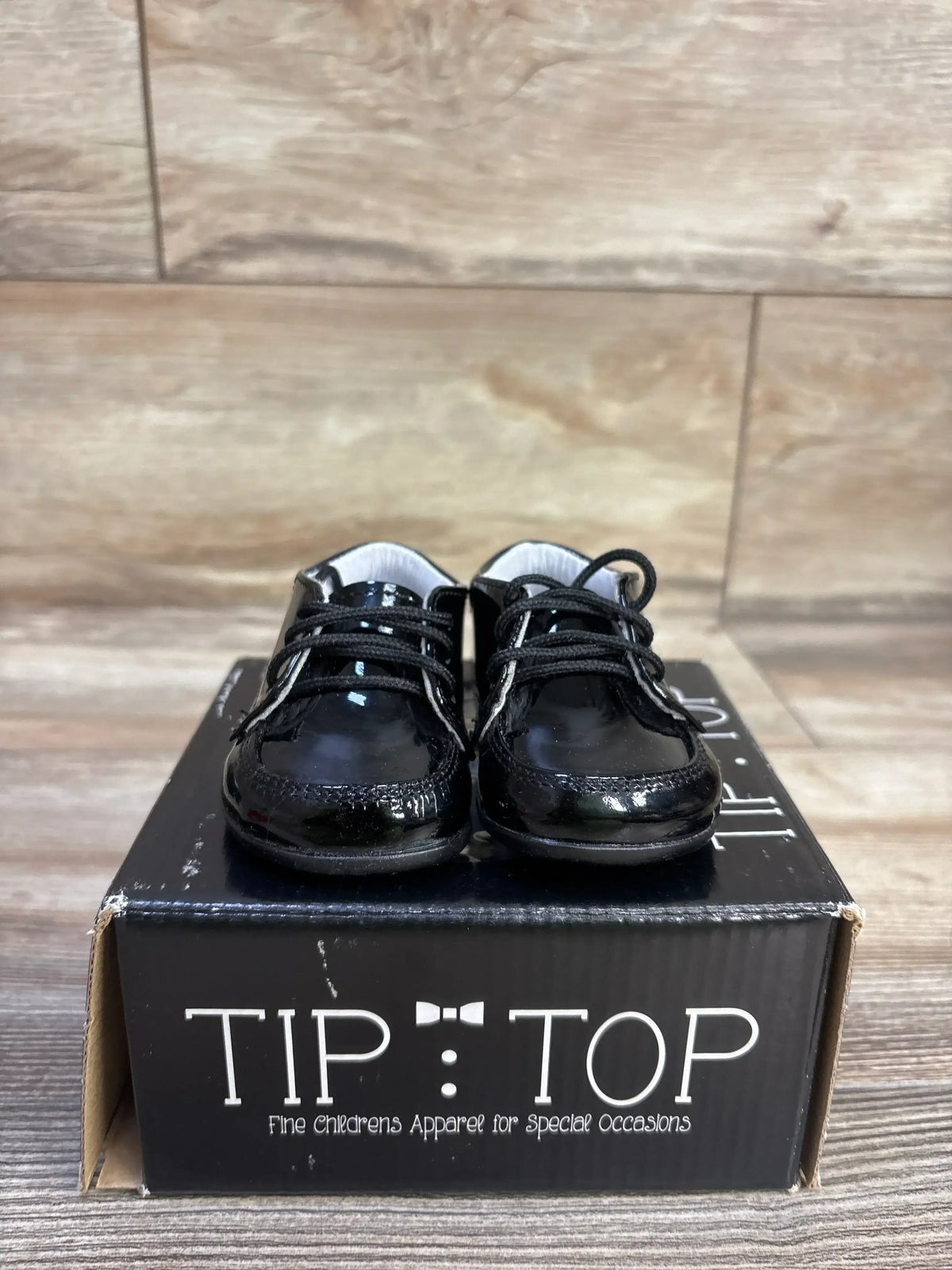 Front view of Tip Top 308 black patent leather sneakers with glossy finish and laces on a Tip Top shoebox on wood floor