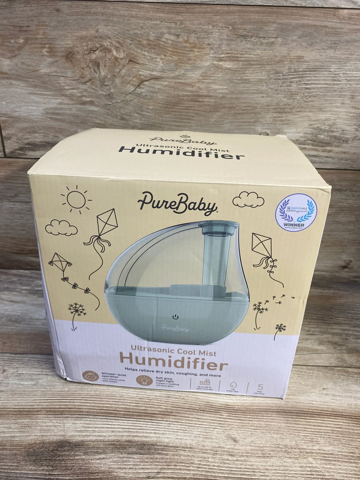 Front view of PureBaby Ultrasonic Cool Mist Humidifier retail box showing the transparent tank and mist nozzle on a wood floor