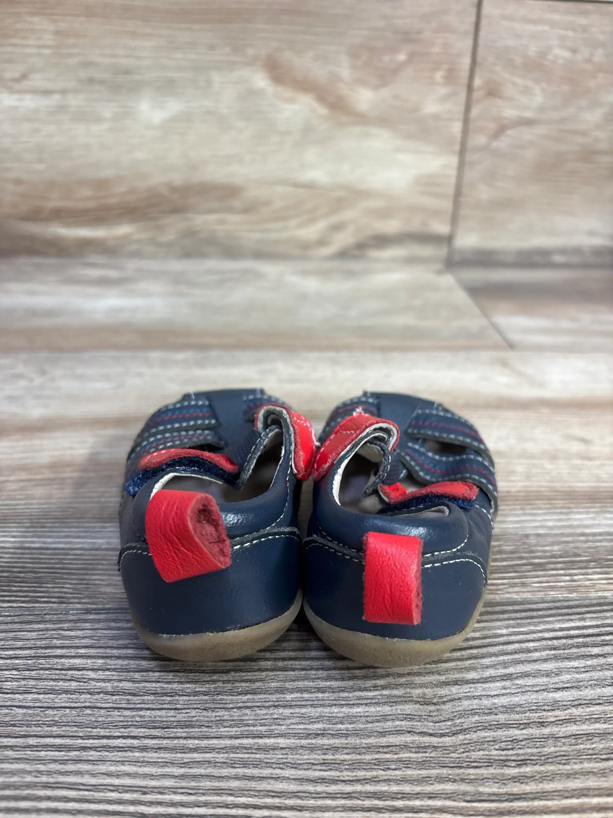 Back view of Smaller By See Kai Run fisherman sandals in navy with red heel pull tab on wood plank floor