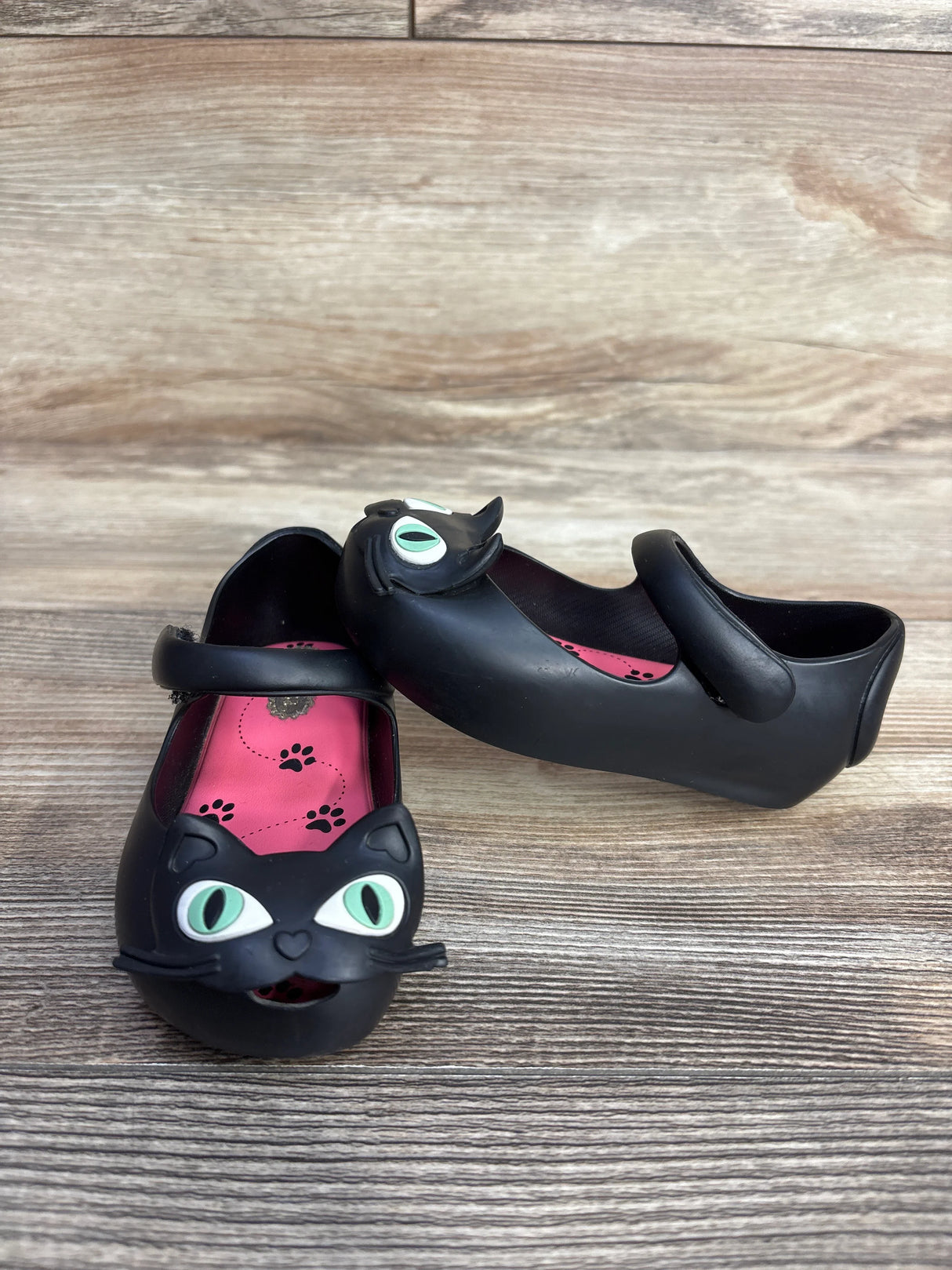 Black children's shoes with cat face design and green eyes on wooden background