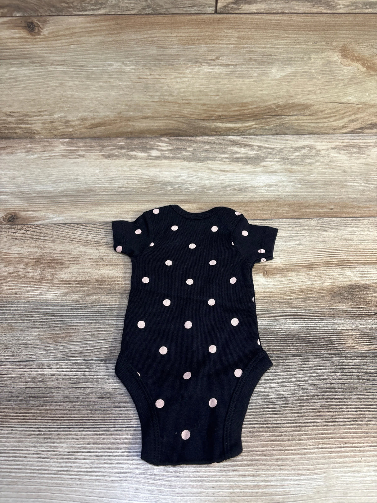 Flat lay of preemie black Gerber polka dot bodysuit showing short sleeves and snap crotch on wood background