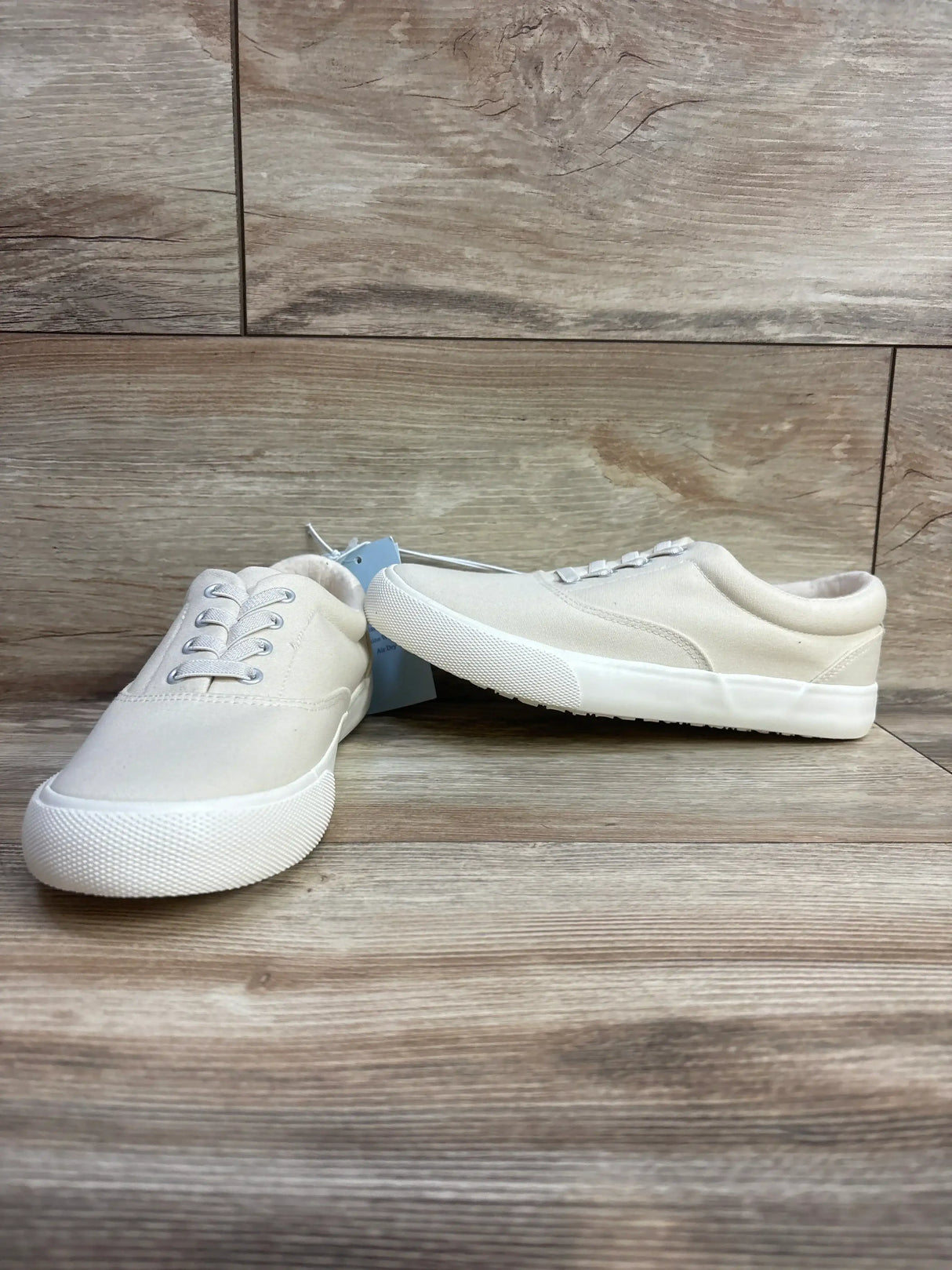 Three-quarter view of Cat & Jack Tyler slip-on sneakers in off-white showing canvas upper and white sole on wood background