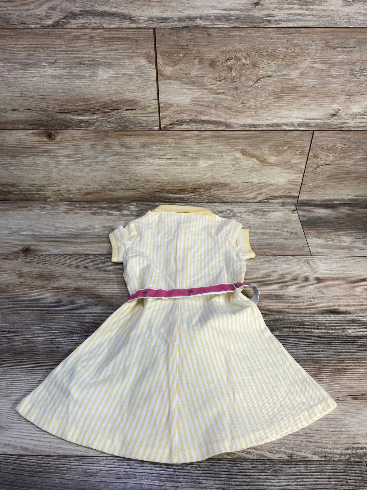 Back view of yellow-and-white striped Polo Ralph Lauren polo dress, pink belted waist and short sleeves on wood background