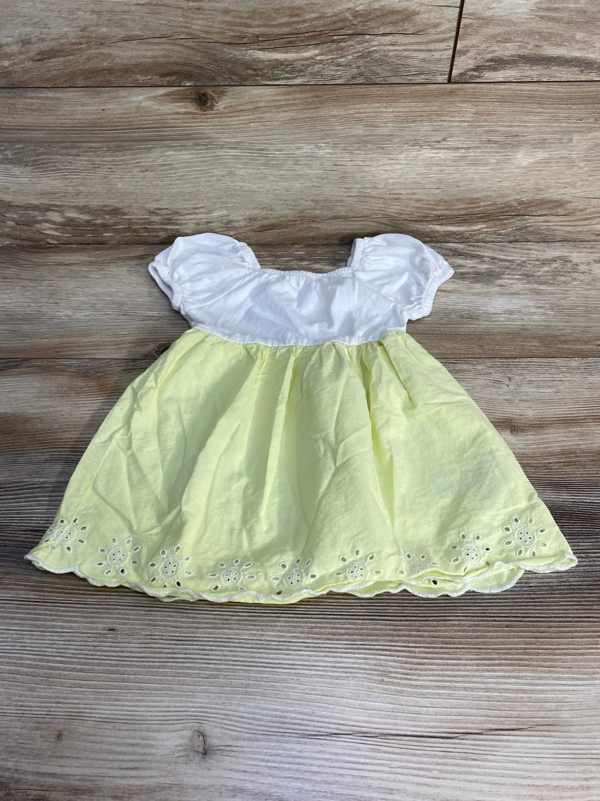 Flat lay of Baby Gap toddler dress size 18-24 months with white puff-sleeve bodice and pale yellow poplin skirt showing scalloped eyelet hem on wood floor