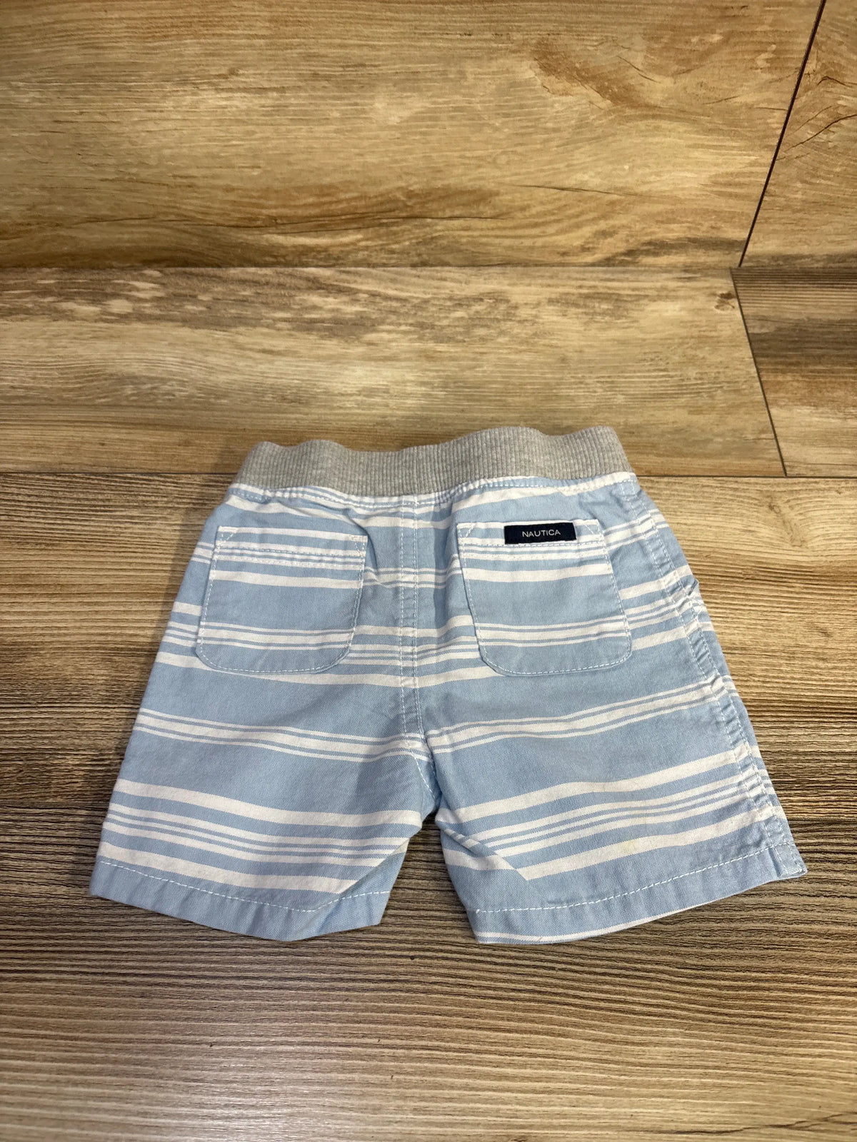 Back view of Nautica striped drawstring shorts in blue showcasing two back pockets on woodgrain