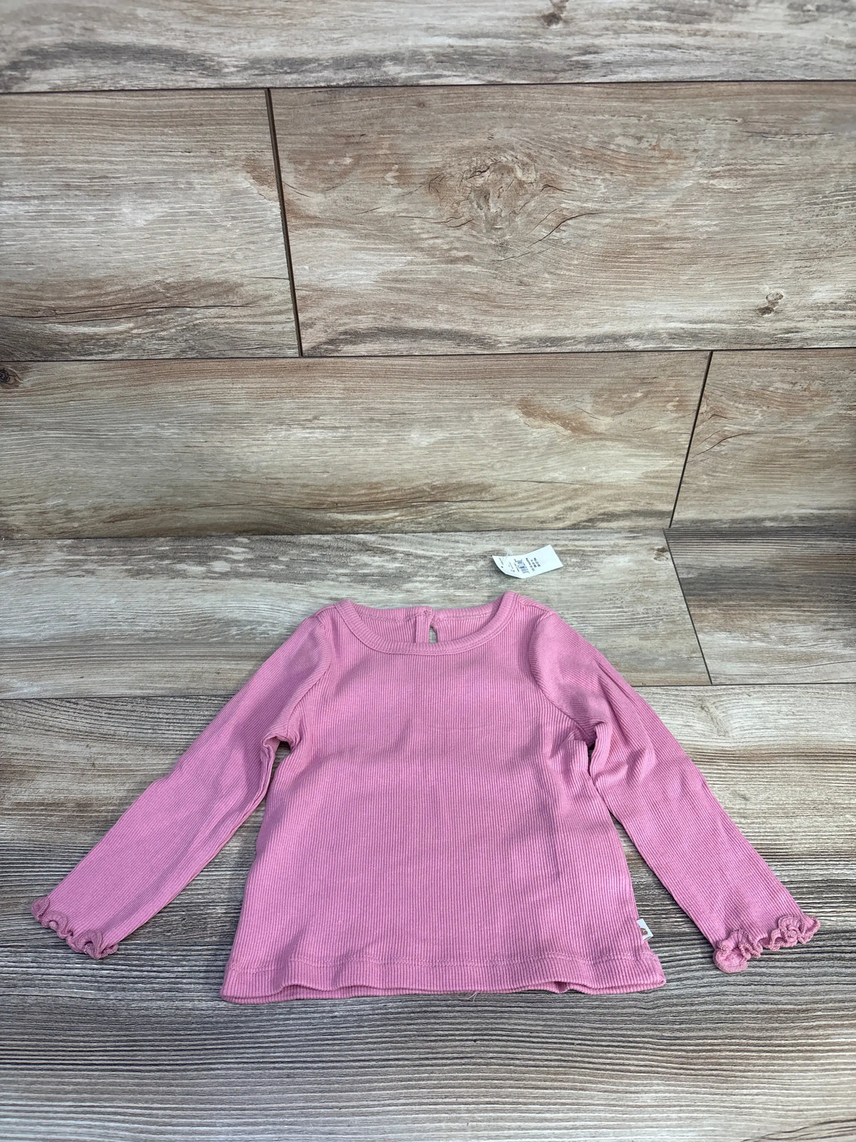 Front view of a pink Baby Gap ribbed long sleeve shirt showcasing lettuce-trim cuffs on a wood-look floor