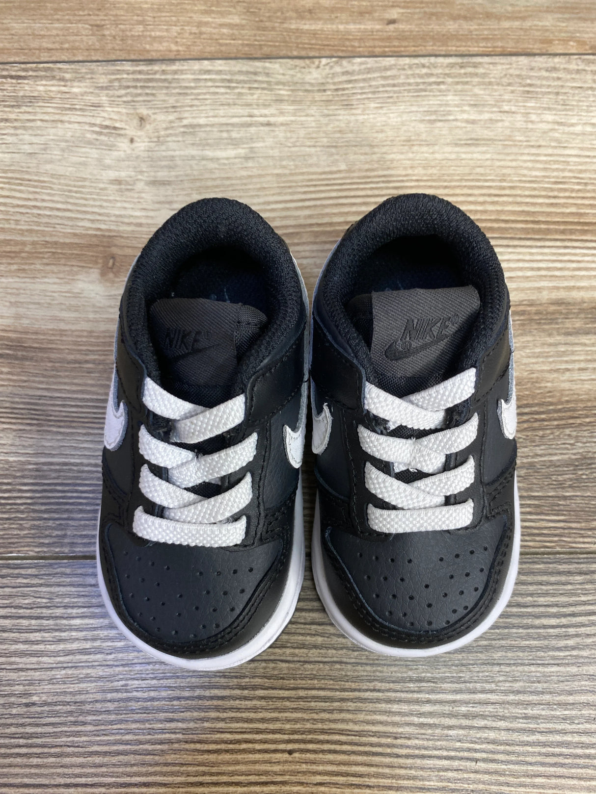 Black and white Nike baby sneakers on wood floor, toddler shoes, kids footwear